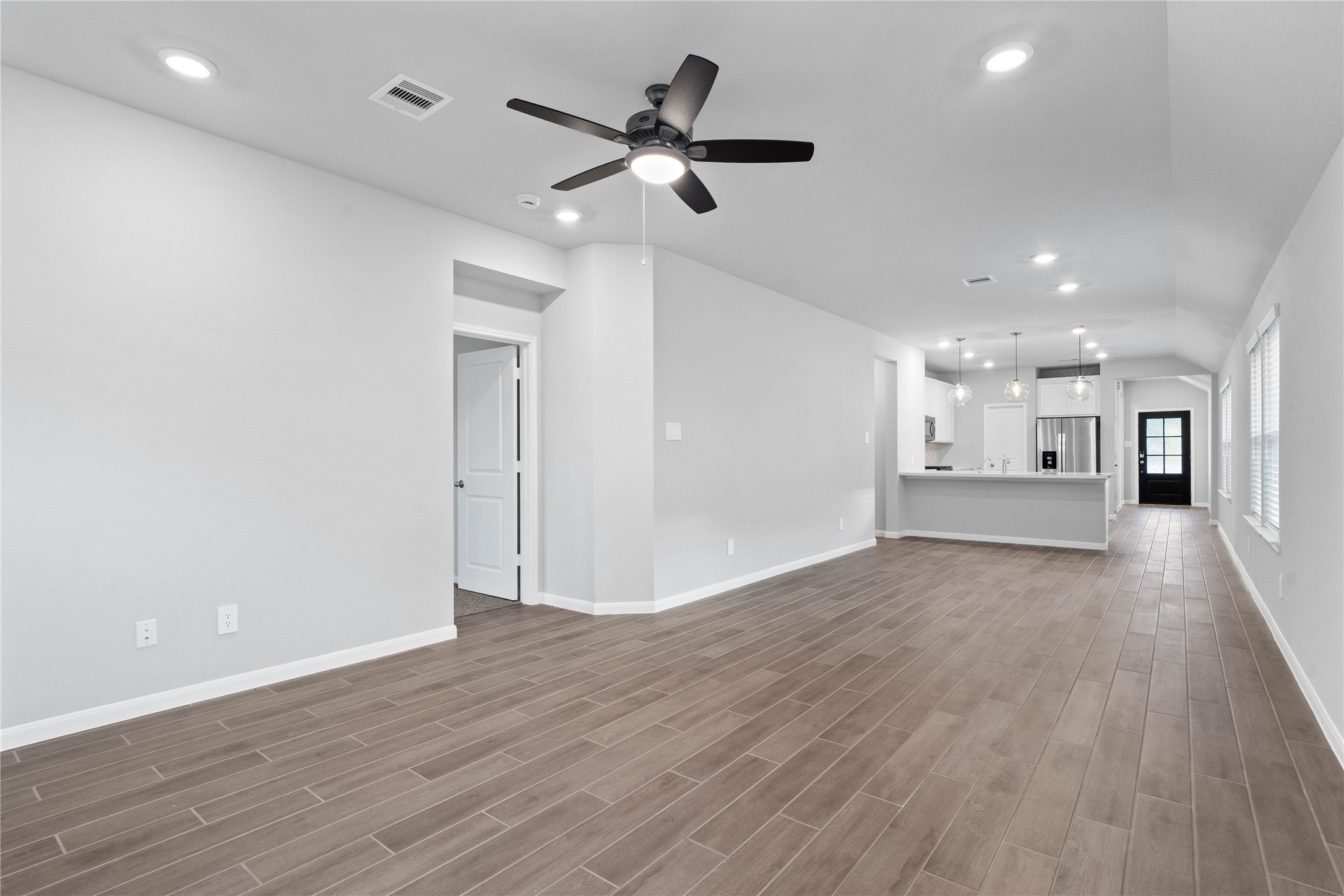 This expansive view from the back of the house showcases a seamless, open-concept layout that creates a warm and inviting path for guests, drawing the eye past the heart of the home toward the welcoming front entryway