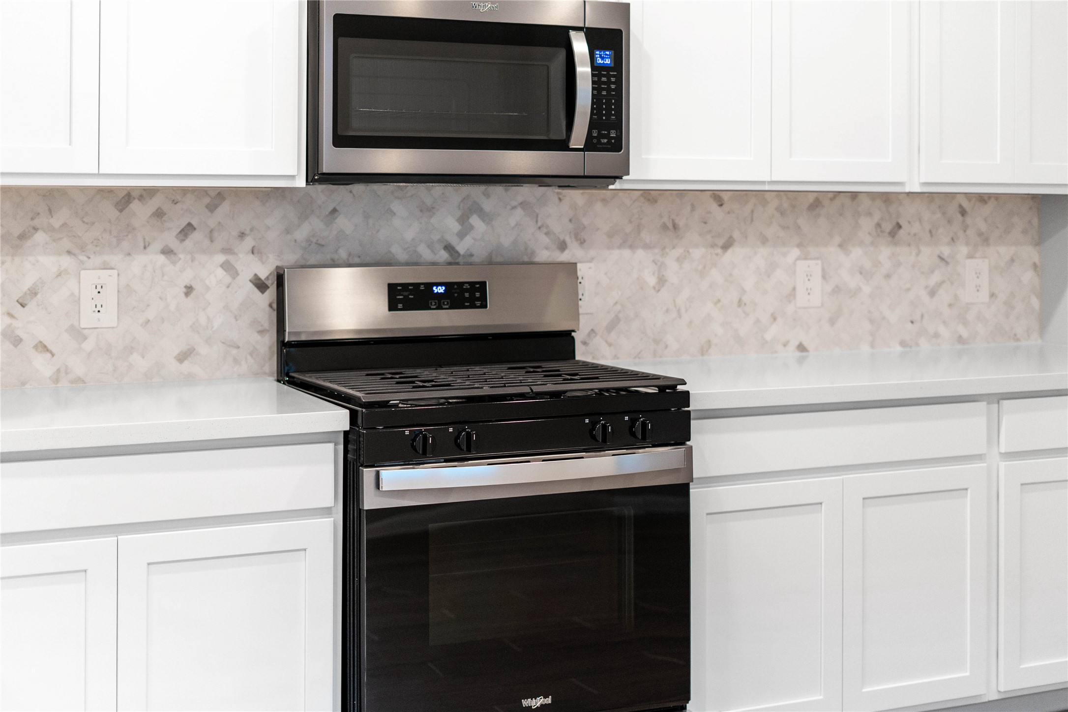Showcased here is a Whirlpool gas range featuring a versatile center oval burner, paired with a steam microwave equipped with sensor cookingall framed by the elegant tile backsplash.