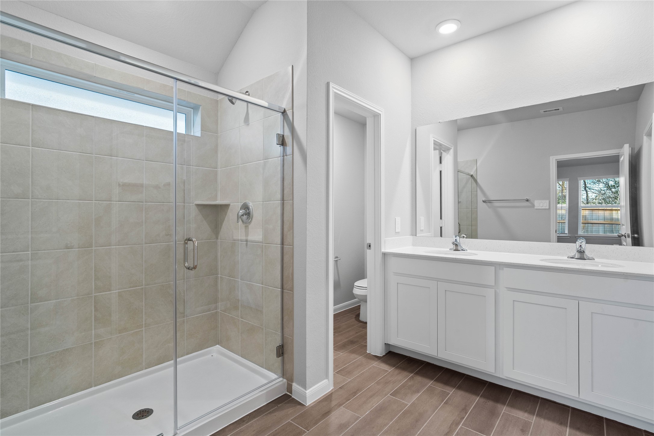 A bright and functional primary bath offering dual sinks for busy mornings, a large mirror, and a modern glass-enclosed shower, creating a serene and efficient space.