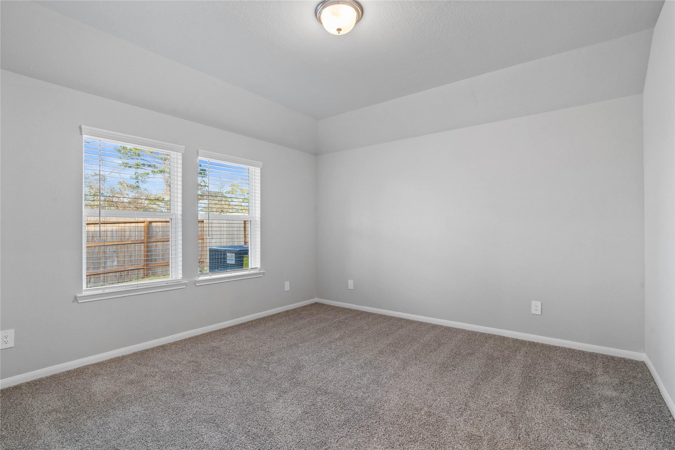 The primary bedroom provides a peaceful escape with a bright, neutral palette, sloped ceilings, large windows, and plush carpet flooring, creating a calm and restorative atmosphere to end your day.