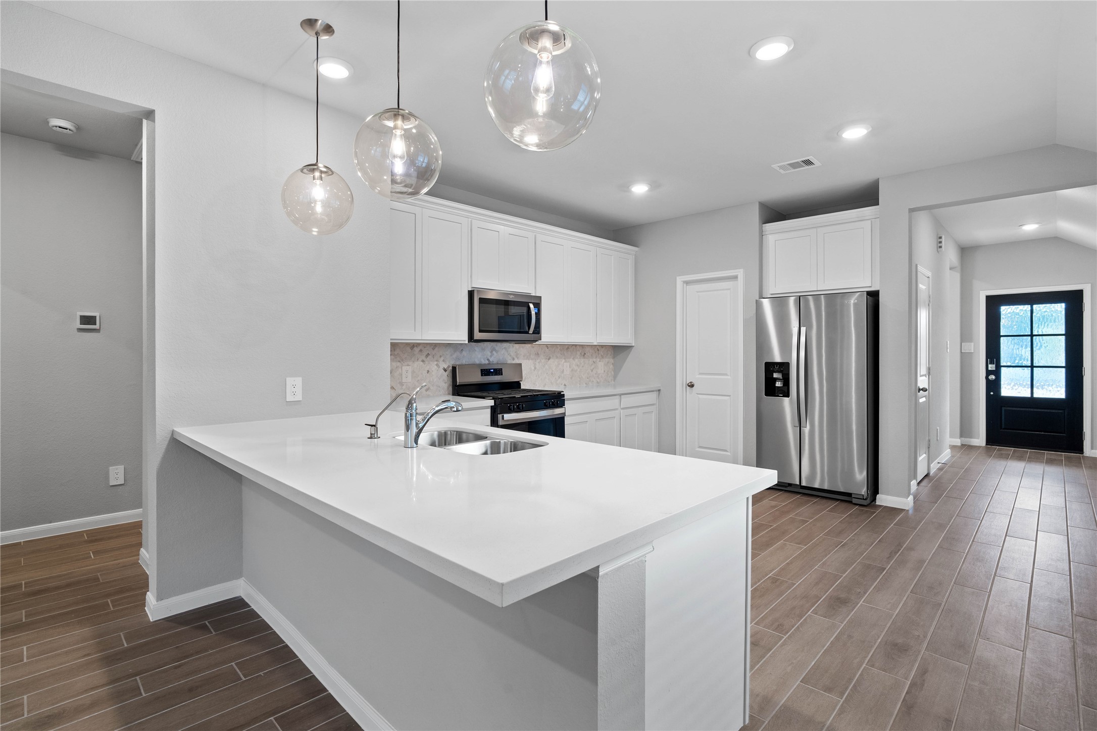 As you step past the entryway, you are immediately welcomed by a bright, open-concept kitchen that serves as the home's focal point. The space feels clean and modern, anchored by a large quartz-topped kitchen counter that seamlessly connects the cooking area to a long, light-filled living space.