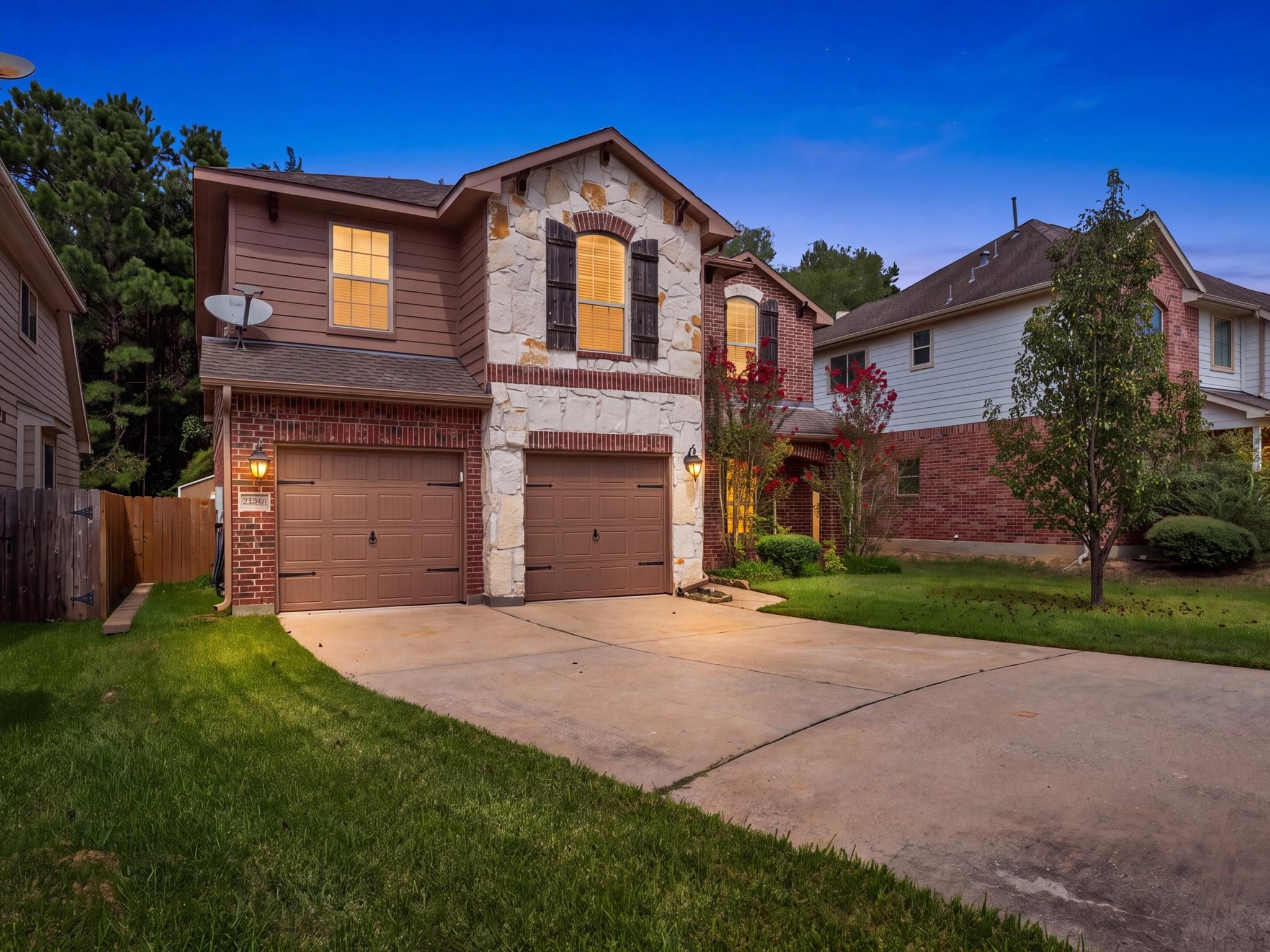 Stunning twilight view highlighting the impressive stone and brick exterior, rustic shutters, and cozy warm interior lighting. Features a spacious concrete driveway, attached two-car garage, and charming front landscaping. Stunning twilight view highlighting the impressive stone and brick exterior, rustic shutters, and cozy warm interior lighting. Features a spacious concrete driveway, attached two-car garage, and charming front landscaping.