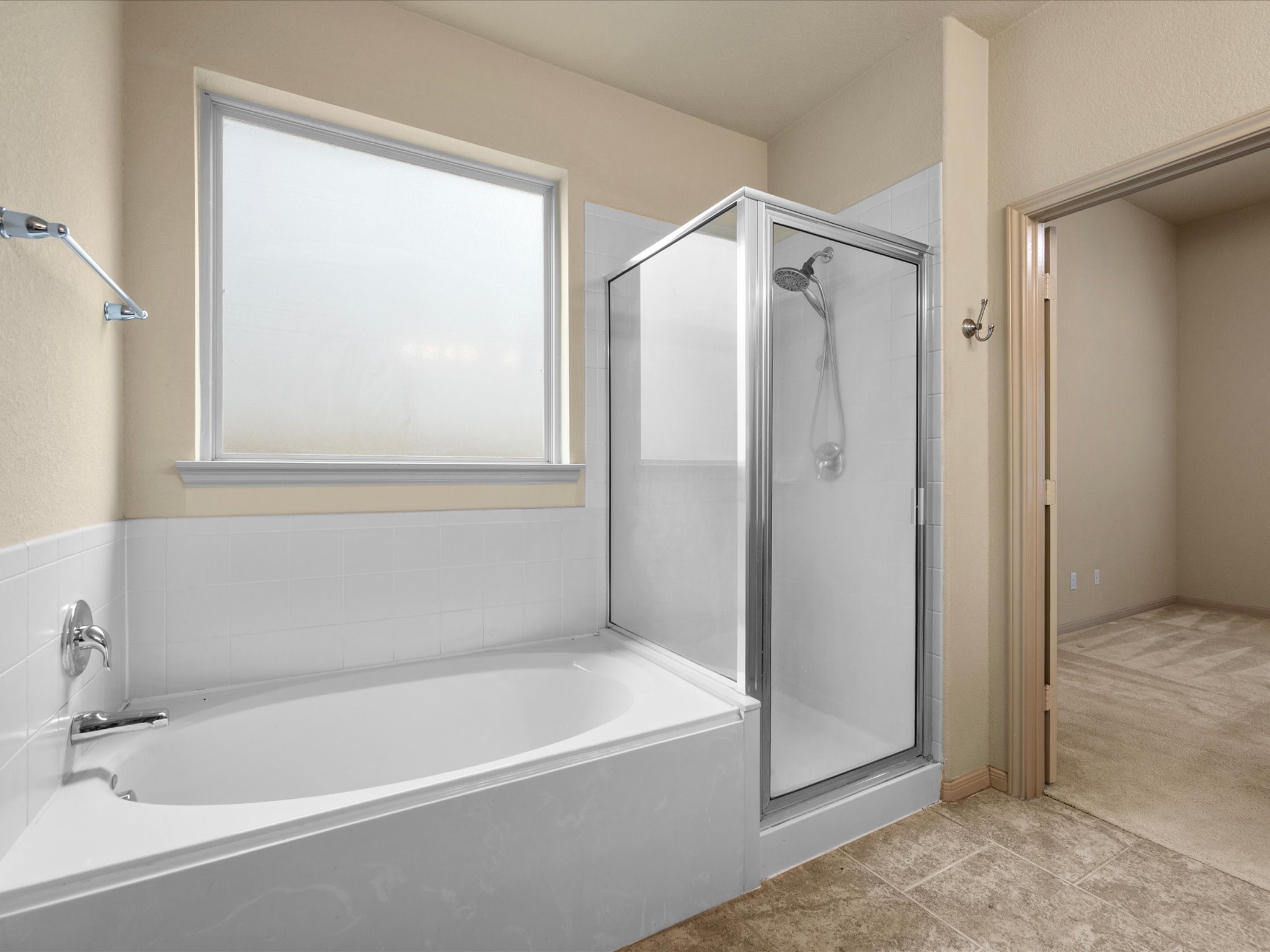 Primary en-suite bathroom featuring a dedicated soaking tub, separate glass-enclosed shower, frosted privacy window for natural light, and durable tile flooring.