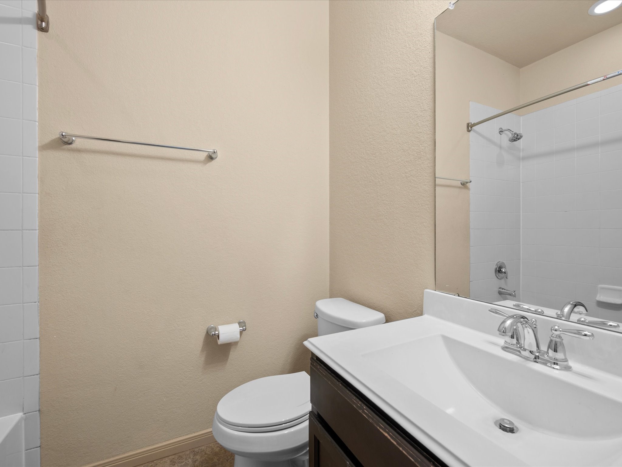 Secondary full bath with a dark vanity, white sink countertop, large mirror, chrome hardware, and a tub/shower combination with tile surround.
