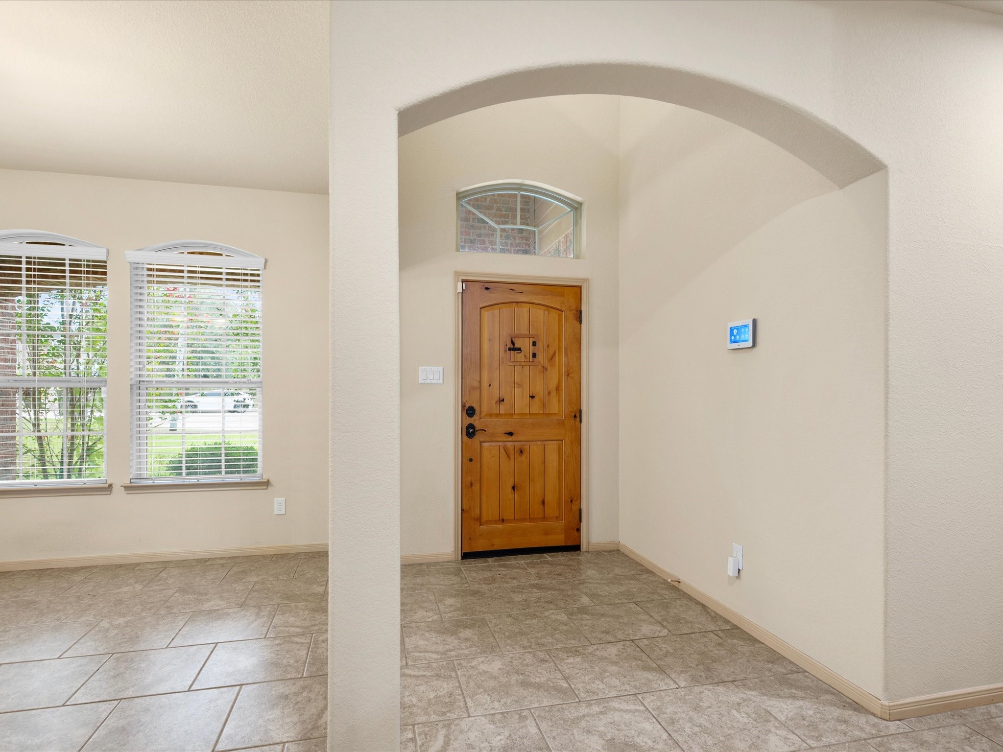 View looking back toward the main entry from the living space, framed by a broad architectural archway. Features low-maintenance tile flooring, high ceilings, a transom window over the front door, and adjacent access to the formal dining area.