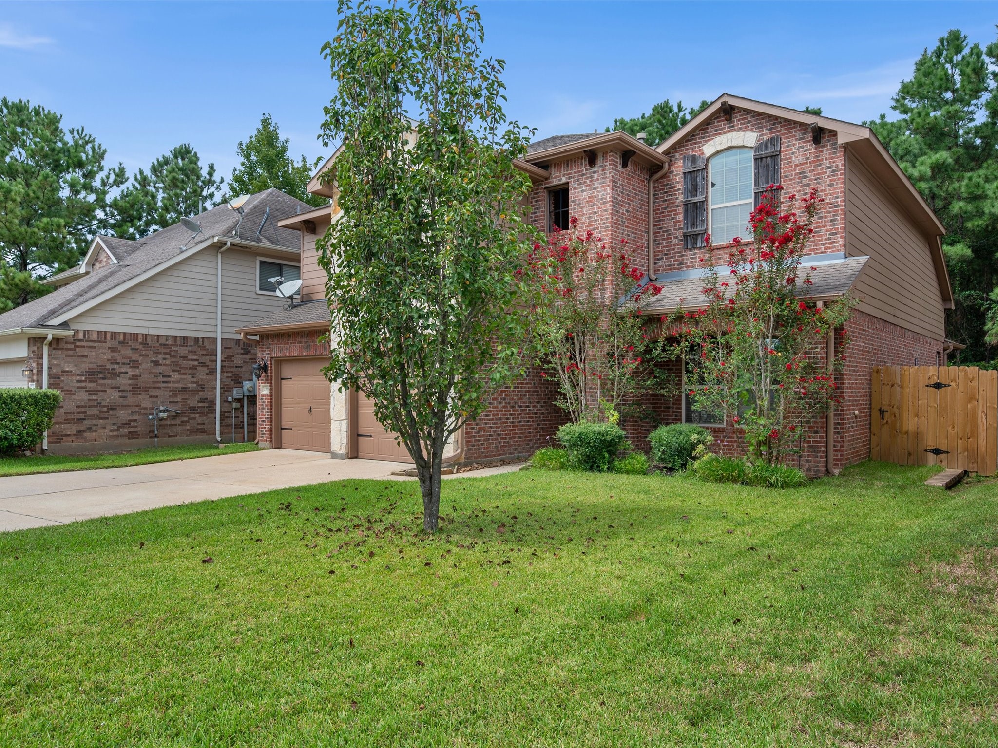 Side-angle view of the front exterior showcasing the classic brick structure, stone accents, vibrant flowering crape myrtles, and a manicured front lawn. Highlights gated side-yard access and mature trees framing the property.