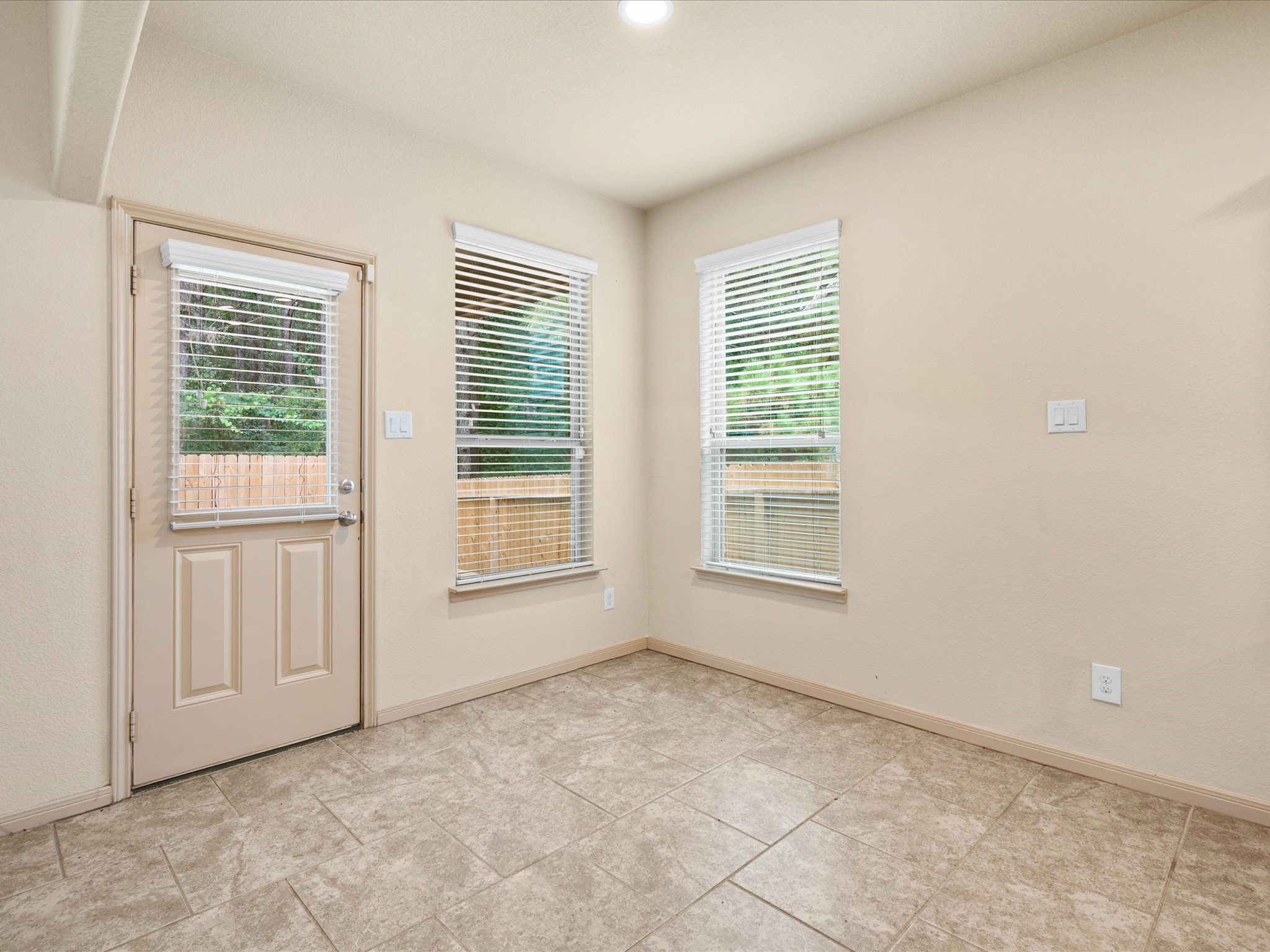 Bright breakfast dining area off the kitchen featuring tile floors, great natural light from dual windows, and direct access to the back patio and newly fenced yard.
