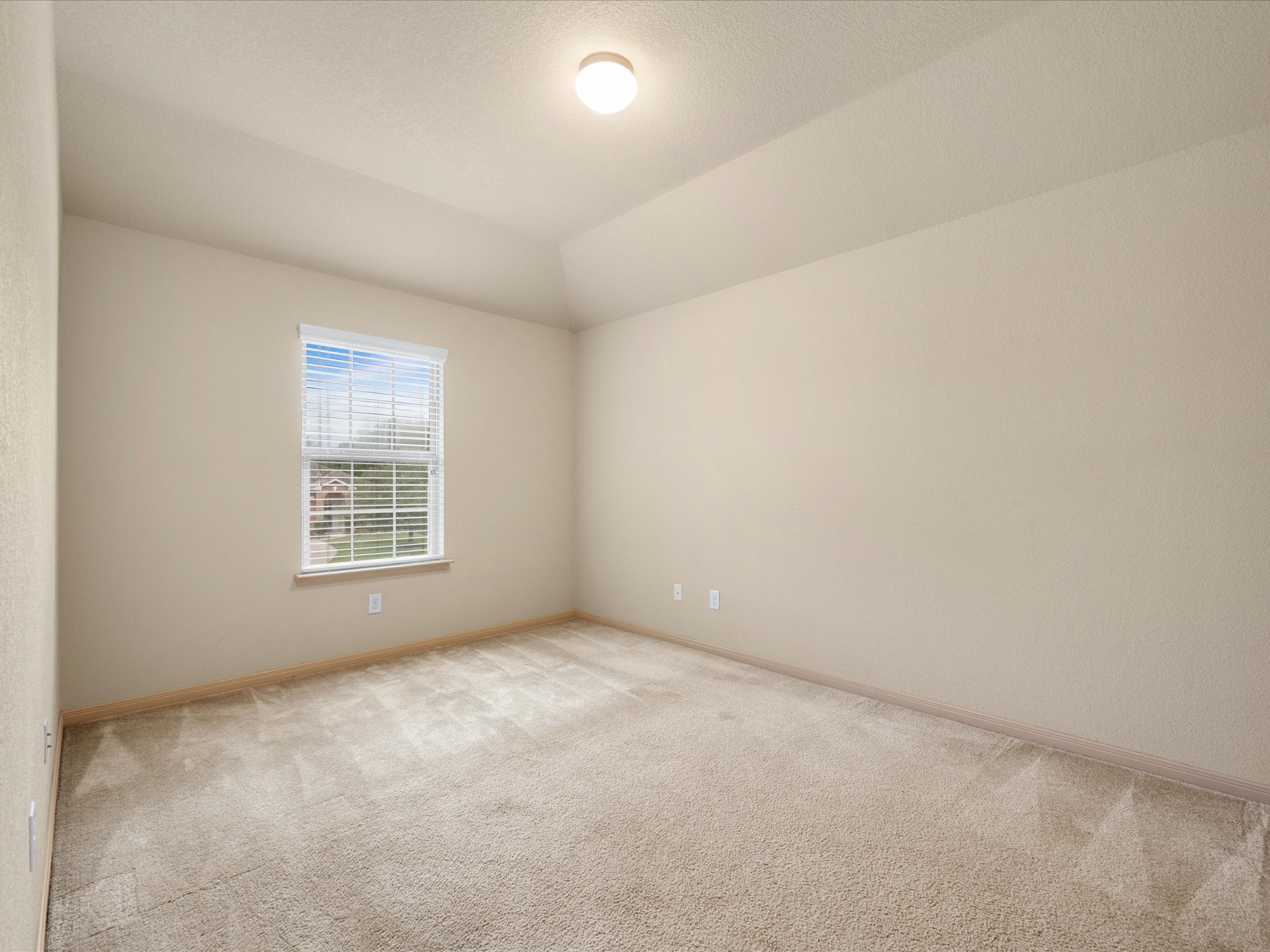 Inviting secondary bedroom featuring high tray ceilings, plush carpet flooring, clean neutral walls, and great natural light from a window with blinds.