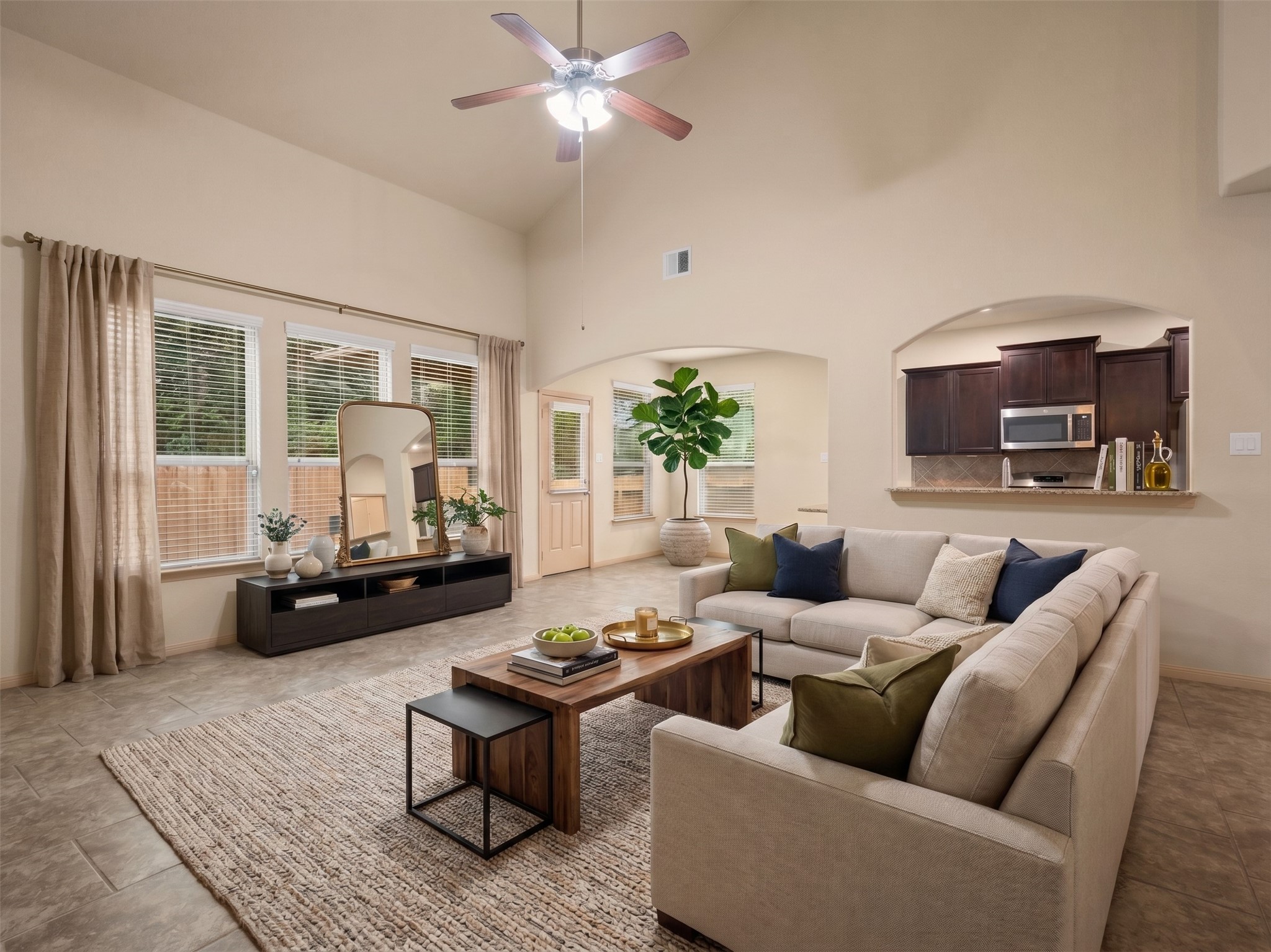 Virtually staged main living room featuring soaring vaulted ceilings, tile flooring, wall of windows with back patio views, and a pass-through bar looking into the kitchen.