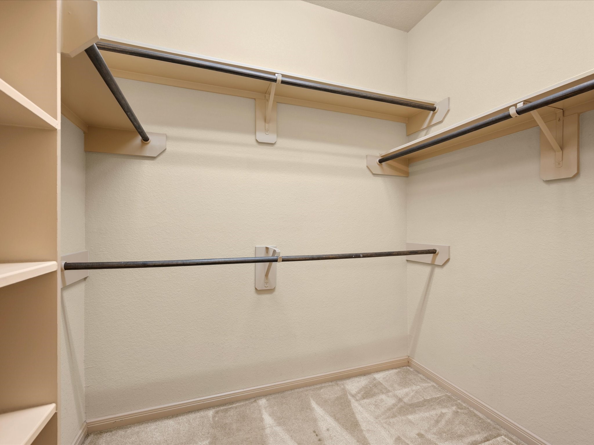 Generously sized primary walk-in closet outfitted with built-in storage solutions. Features multi-level hanging rods to maximize vertical space, upper shelving for folded items or storage bins, built-in cubbies/shelving, and soft carpet flooring.