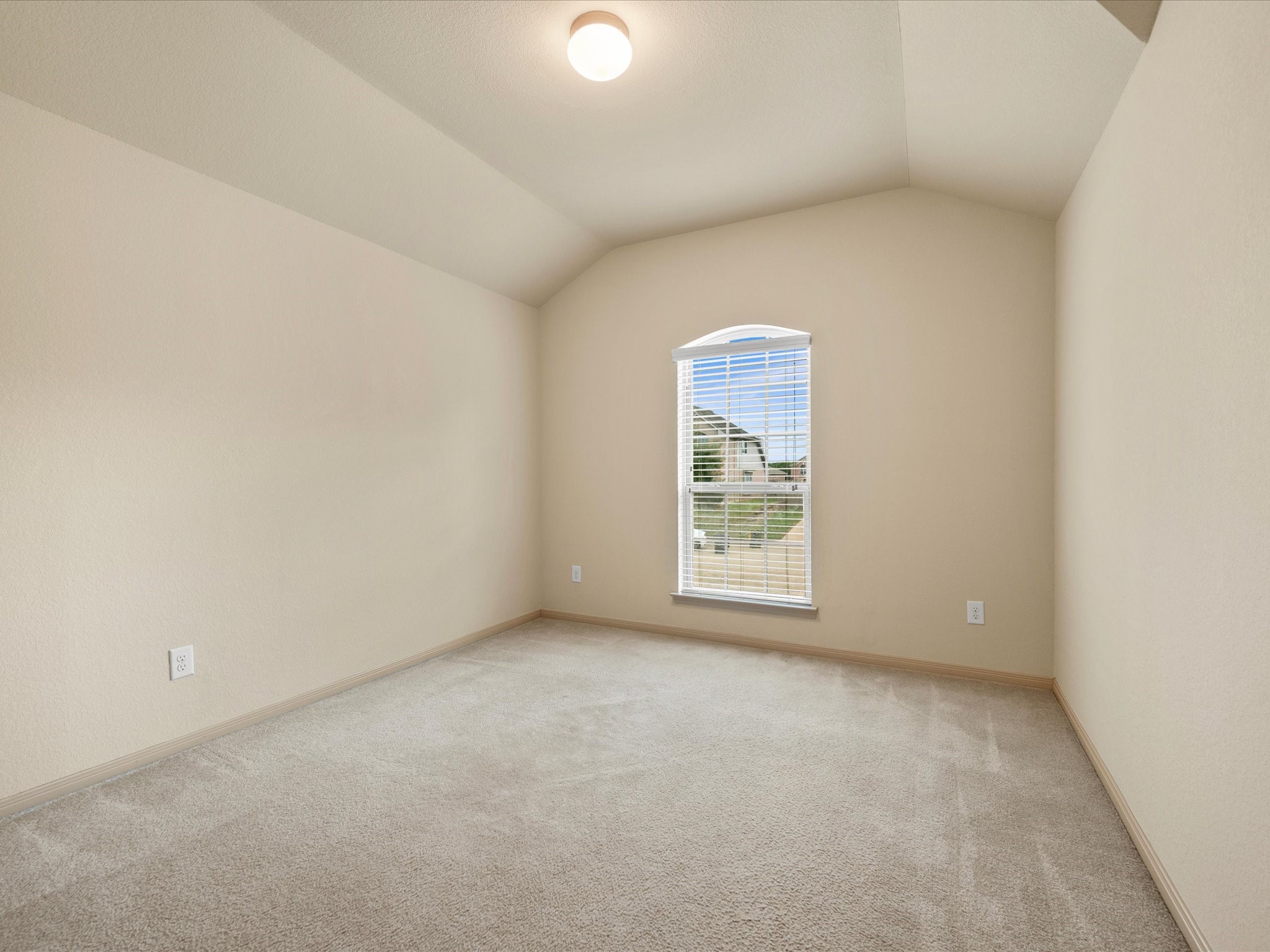 Secondary bedroom featuring dramatic vaulted ceilings, plush carpeting, neutral finishes, and a focal arched window providing abundant natural light.