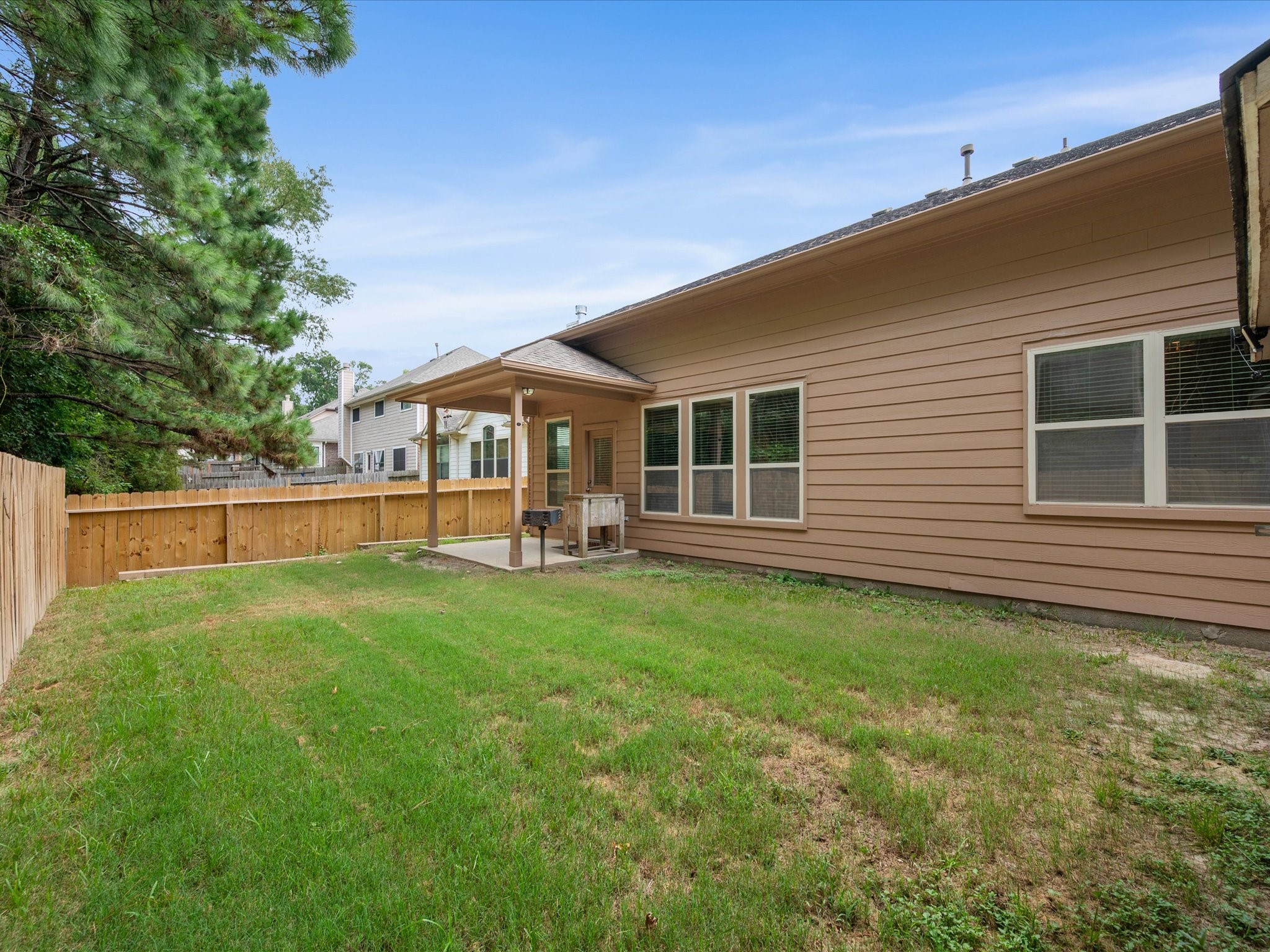 Spacious, private backyard featuring a covered patio, wooden privacy fencing, lush mature trees bordering the rear lot line, and a large lawn space.