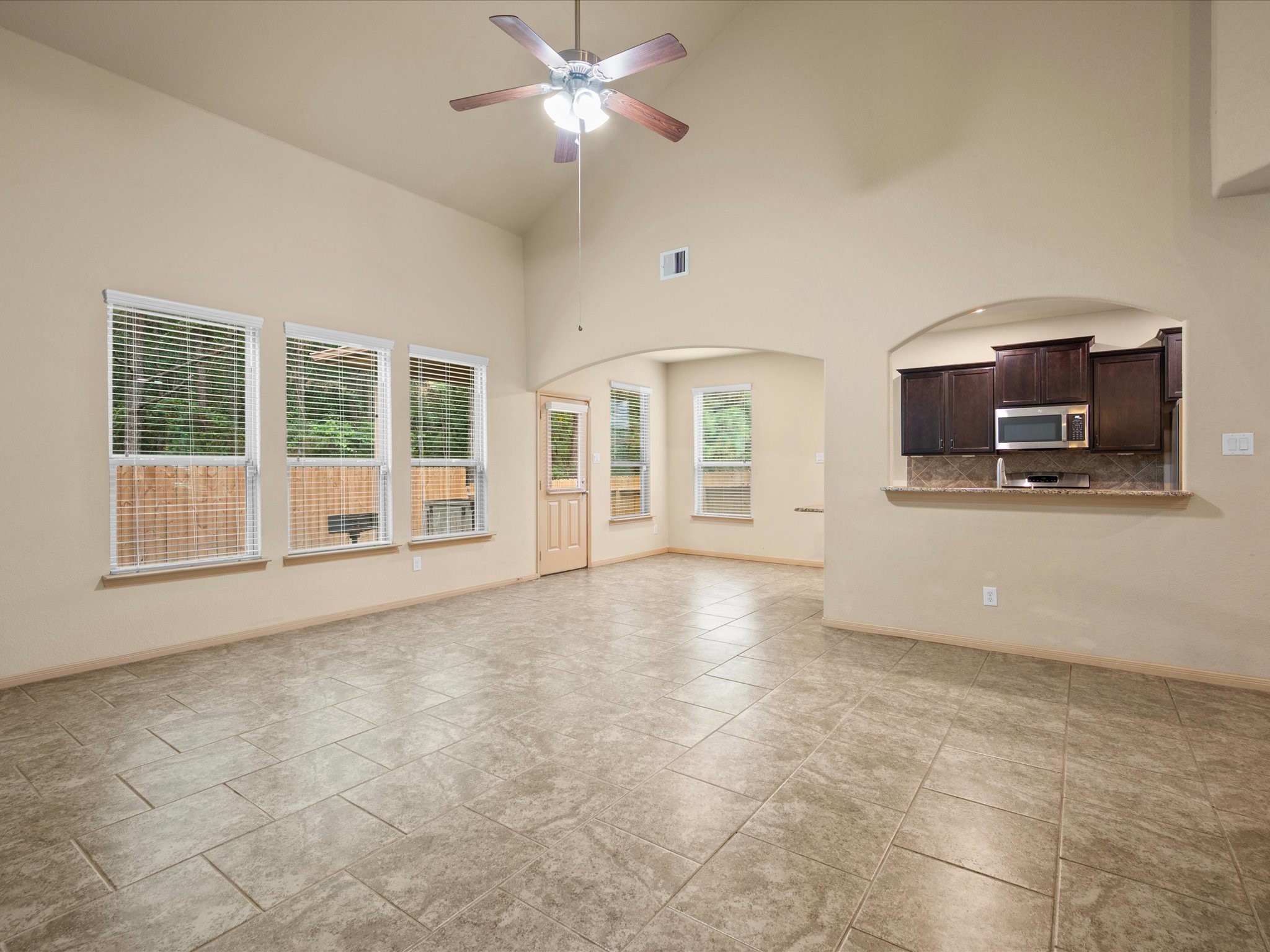 Expansive living room demonstrating the home's open-concept design, vaulted ceilings with a light fixture fan, and tile flooring. Showcases the arched pass-through window into the kitchen, perfect for entertaining and seamless transition into the breakfast nook.