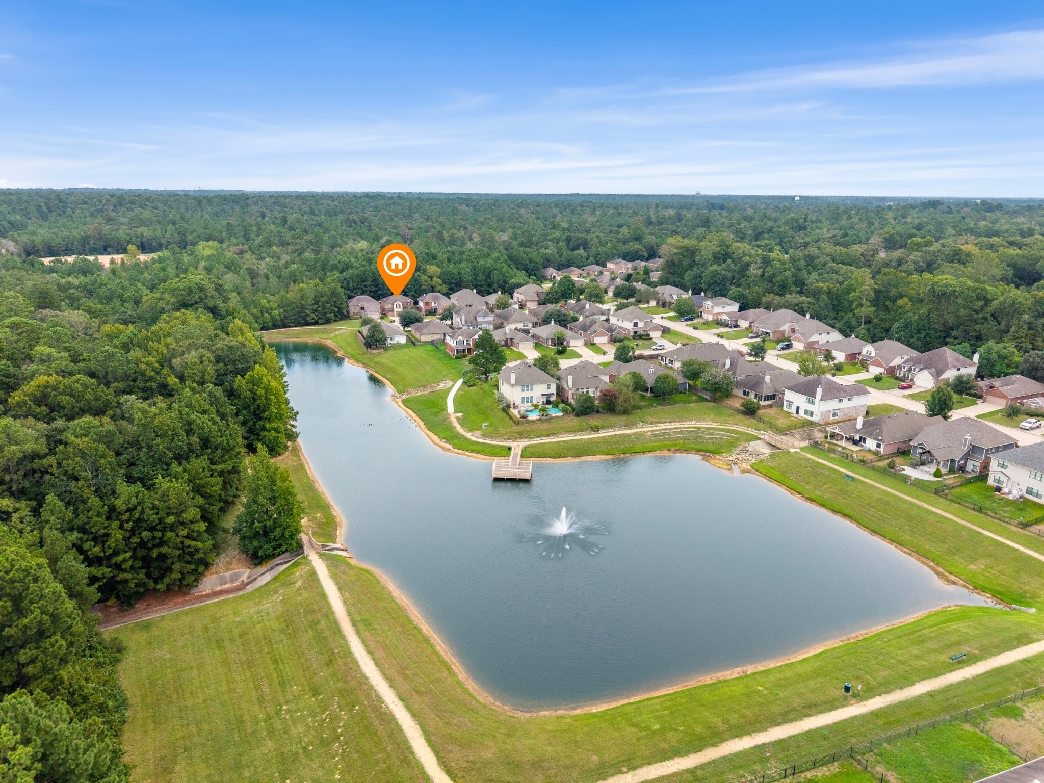 Expansive aerial view showcasing the home's premier position near the neighborhood lake, walking paths, and fountain, all backed by miles of dense green forest reserve.