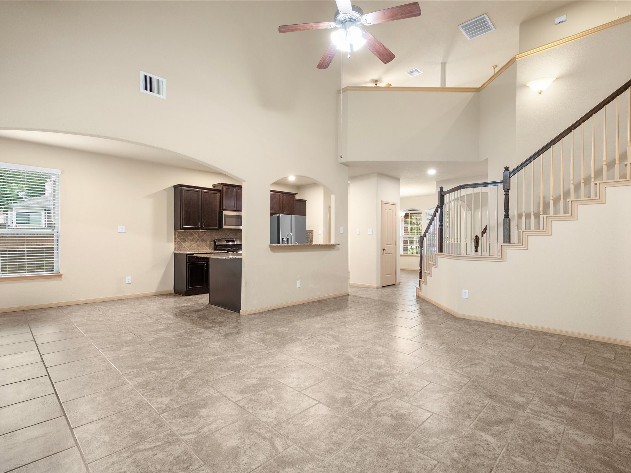Wide-angle perspective of the main living space showcasing the dramatic two-story vaulted ceilings, overhead ceiling fan, and open staircase leading to the game room loft. Highlights the seamless open layout connecting the family room, kitchen, and foyer.