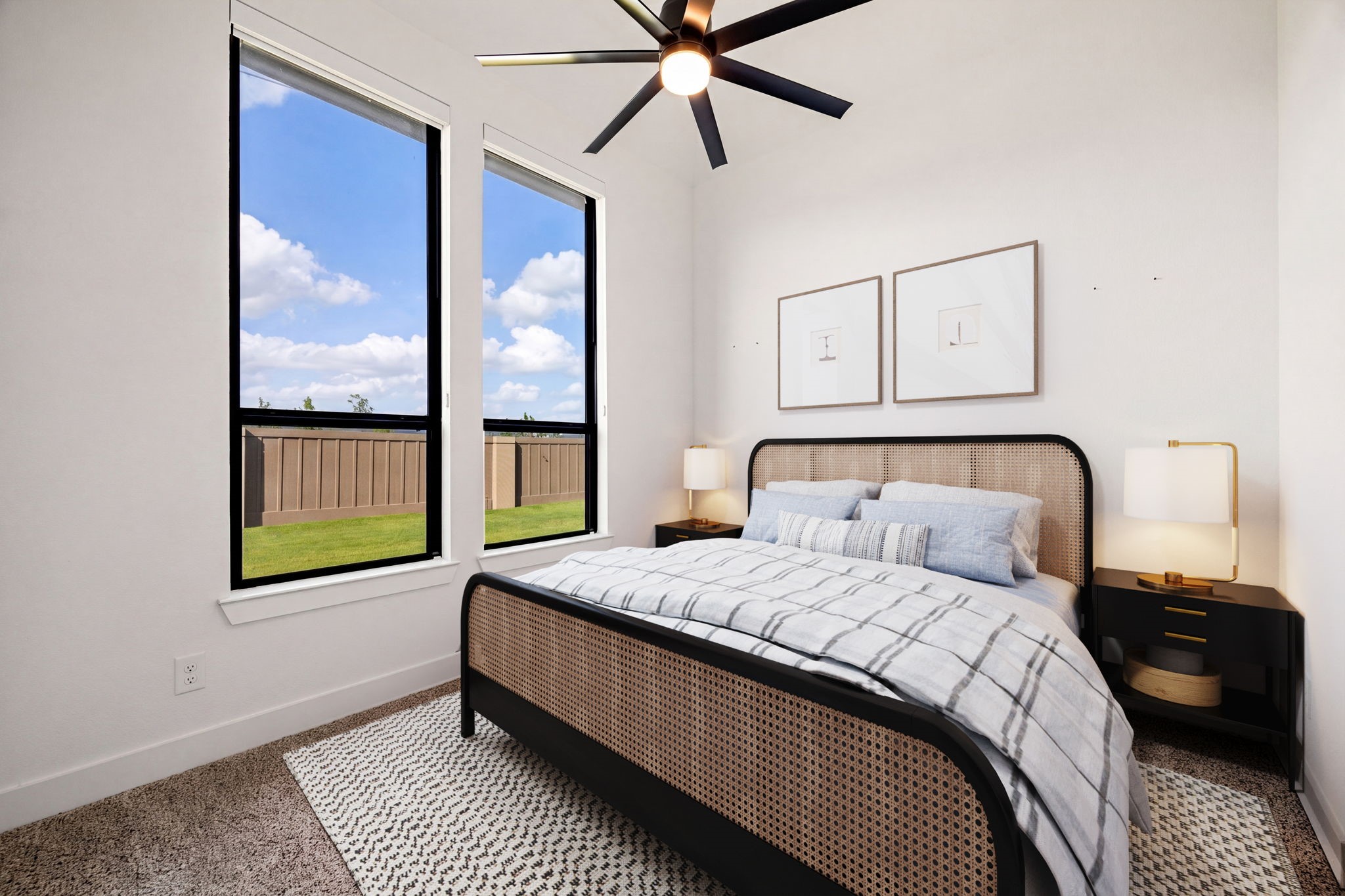 A bright and inviting guest retreat. Two tall, black-trimmed vertical windows with pull down black out shades pull in abundant natural light, beautifully accentuating the home's high-end wide-plank flooring, crisp neutral walls, and modern multi-blade ceiling fan.