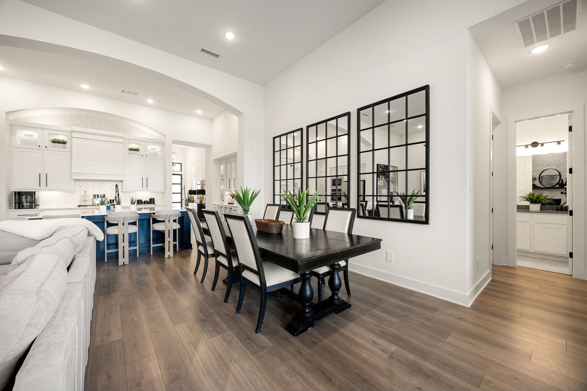 An effortlessly connected layout. The elegant dining space transitions seamlessly into both the gourmet kitchen and the main living area, highlighted by wide-plank flooring, clean lines, recessed lighting, and a view into a private hallway nook.