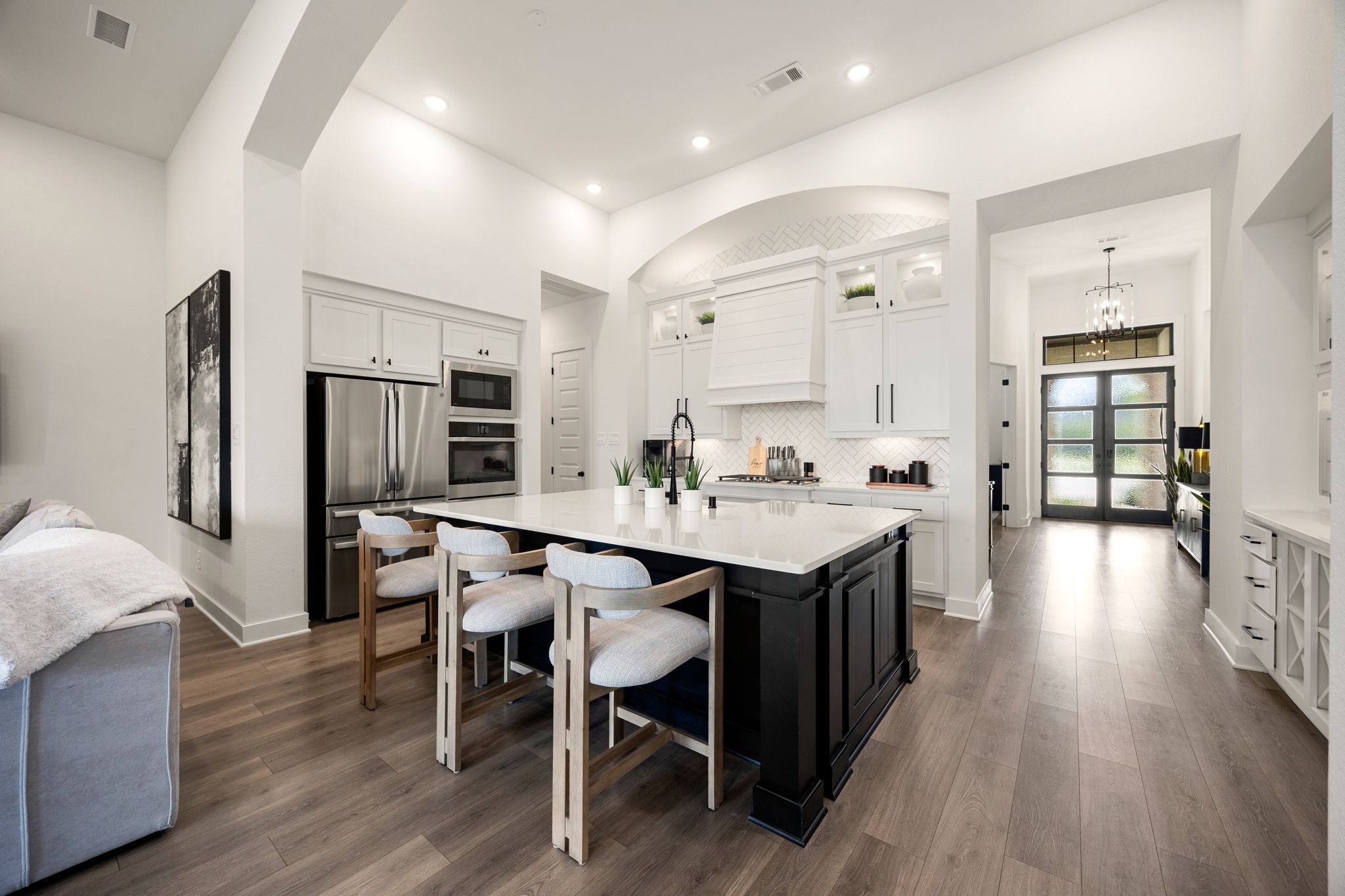 A true chefs dream. This spectacular kitchen centers around a massive dark wood island with crisp white quartz countertops, beautifully accented by a custom range hood, premium stainless steel built-in appliances, pristine recessed lighting, and a dramatic arched entry leading back to the bright foyer.