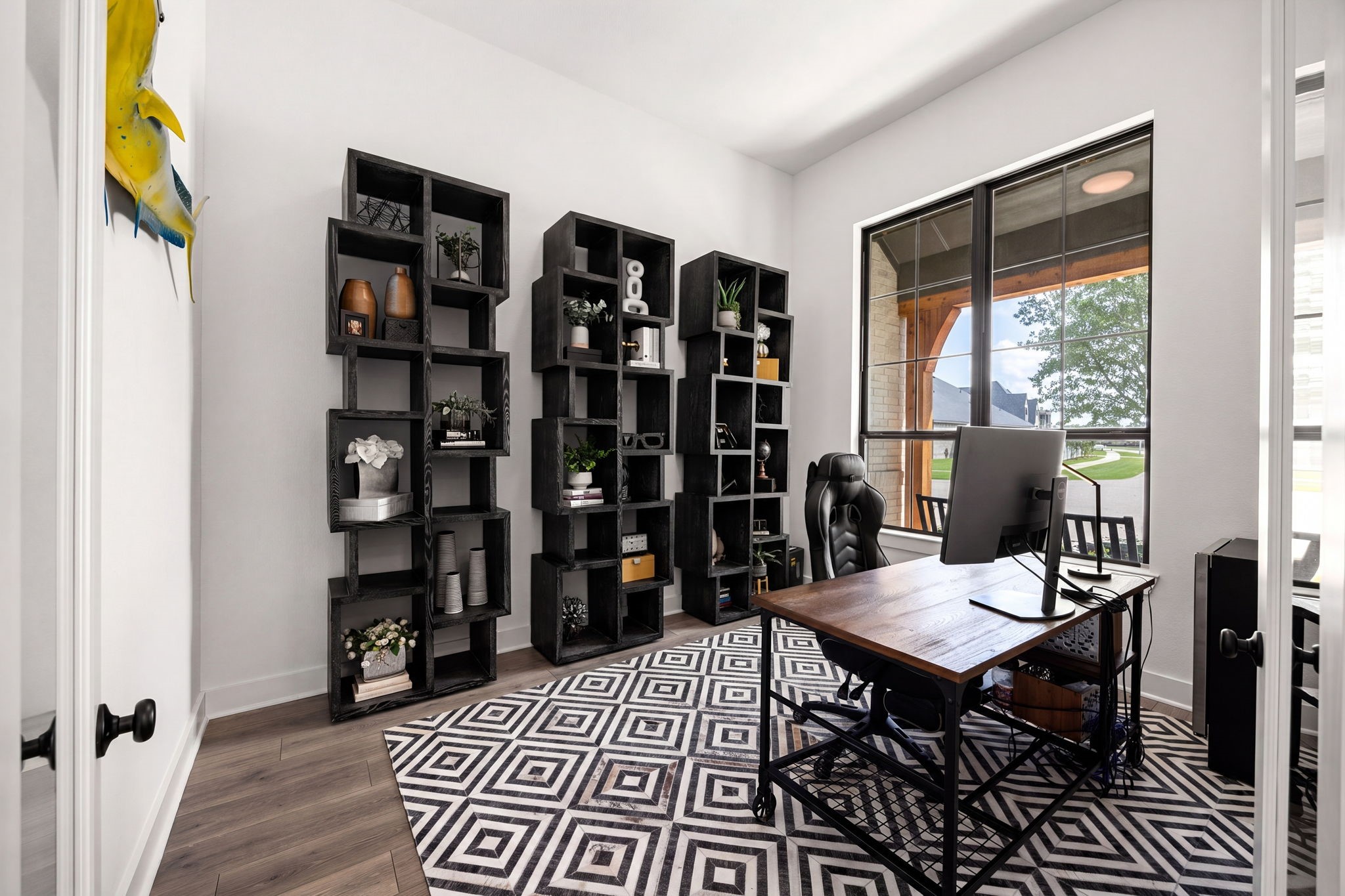 An inspiring dedicated home office. High-end wide-plank flooring spans this bright workspace, complete with towering windows framing outdoor views, clean neutral walls, and matte black door hardware.