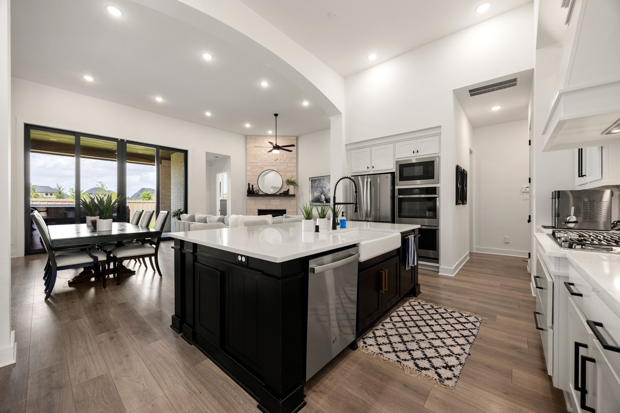 Seamless entertaining at its finest. This multi-angle perspective highlights the massive island with an integrated stainless steel dishwasher, an undermount apron-front farmhouse sink, a premium gooseneck faucet, and wide glass doors leading to the outdoor living area.
