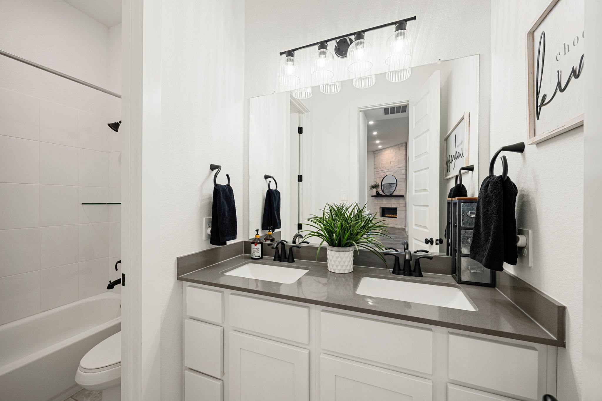A crisp and functional secondary bath. White shaker-style cabinetry is paired with premium grey countertops, dual undermount rectangular sinks, matte black fixtures, modern vanity lighting, and a clean tub-and-shower combination.