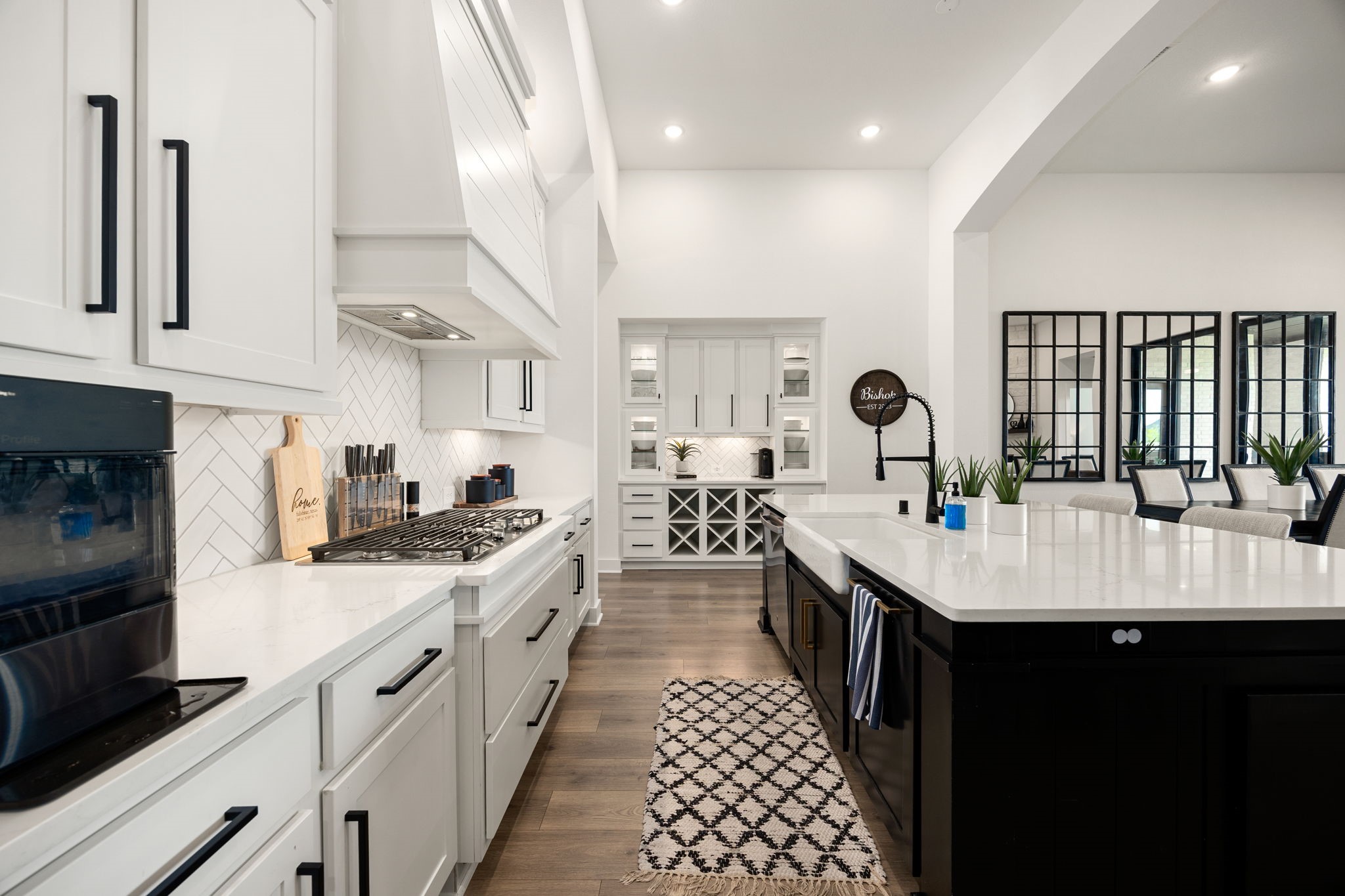 Flawless kitchen design and details. Modern matte black hardware accents the floor-to-ceiling white cabinetry, perfectly contrasting with the dark wood island, a striking custom range hood, sleek recessed lighting, and a durable undermount farmhouse sink.