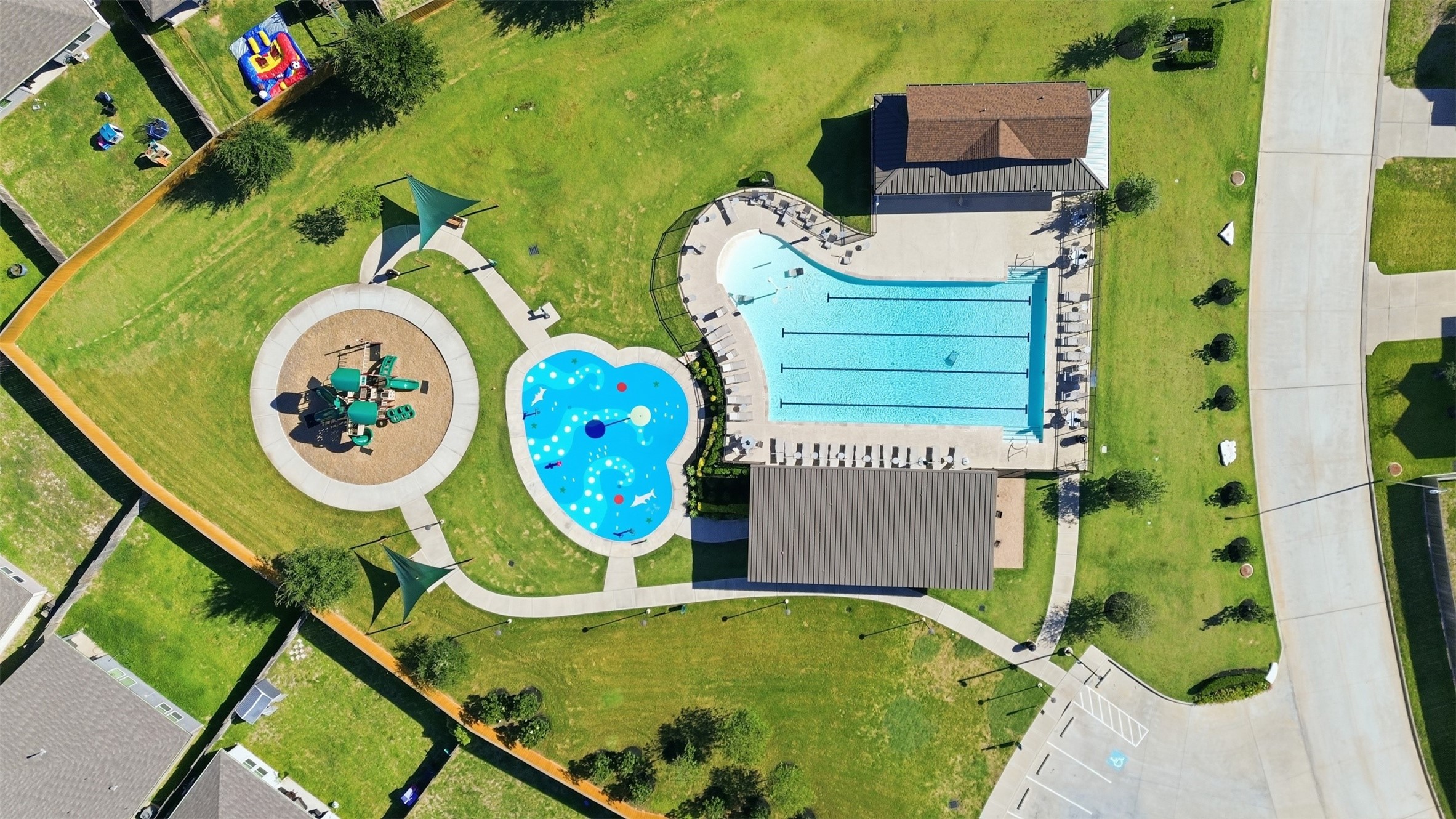 Discover a vibrant community space featuring a large pool with lap lanes, a playful splash pad, and a well-equipped playground, all surrounded by lush green lawns and shaded seating areas.