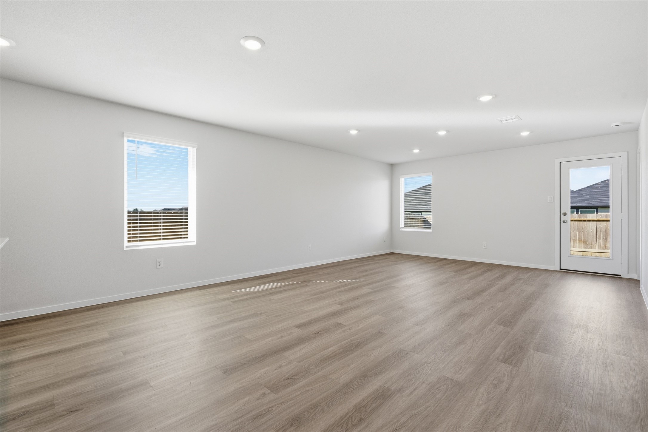 Spacious and bright living area with sleek hardwood floors, recessed lighting, and ample natural light through large windows, offering a modern and inviting atmosphere.