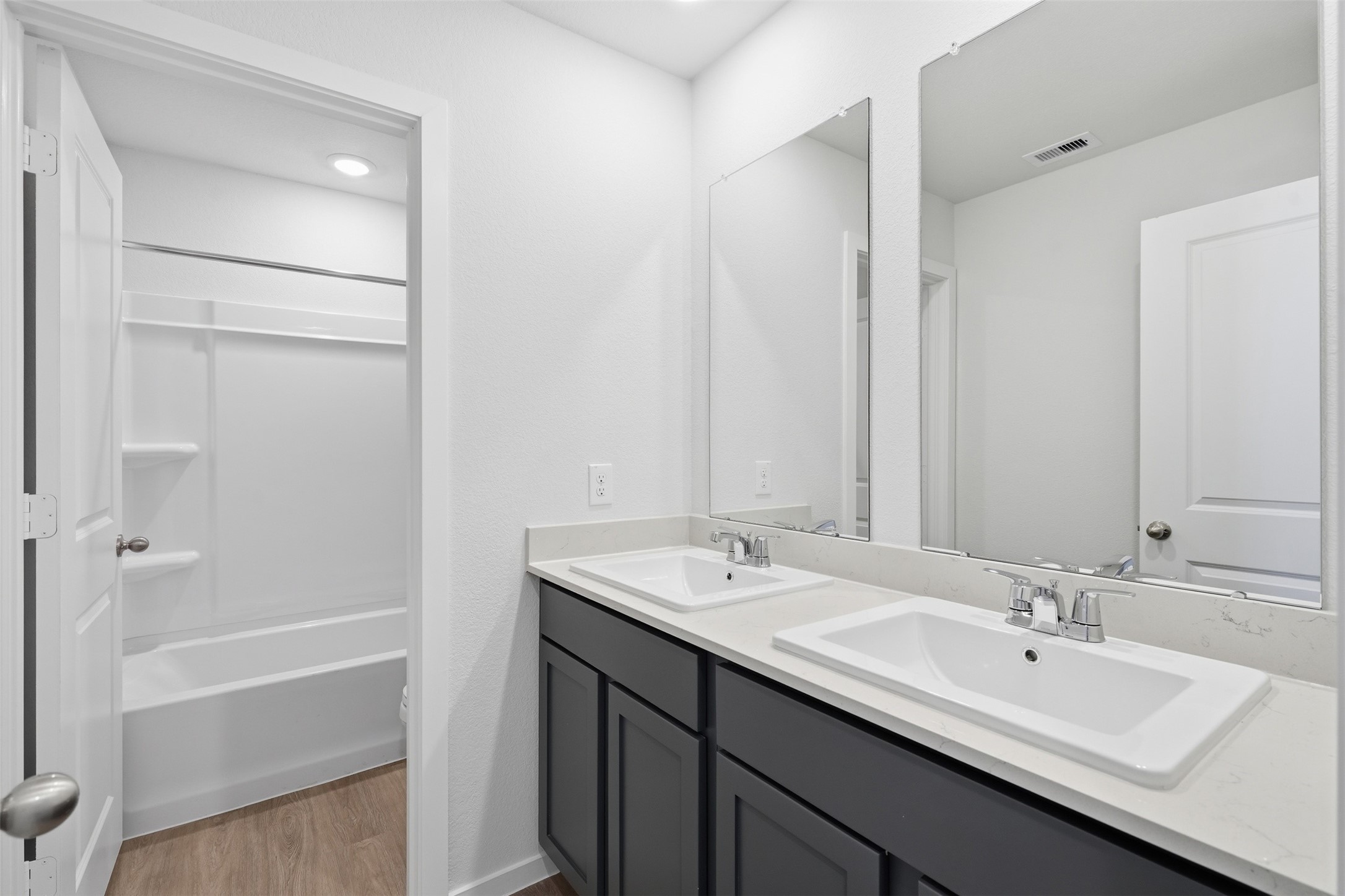 Modern bathroom featuring dual sinks with sleek fixtures, spacious vanity mirrors, and a separate bathtub area with a contemporary design.