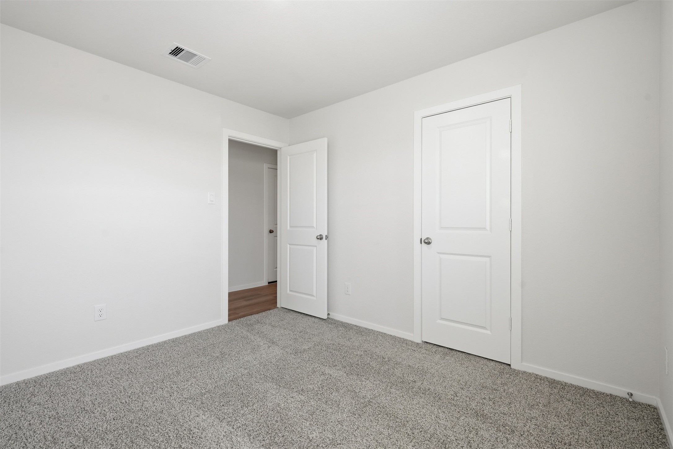 Bright and inviting room with soft carpet flooring, neutral walls, and dual doors for easy access and storage.