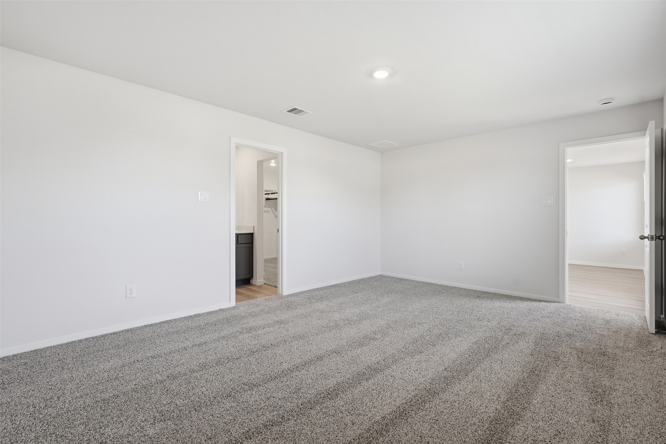 Spacious bedroom with soft carpet flooring, ample natural light, and convenient access to a modern en-suite bathroom and walk-in closet.
