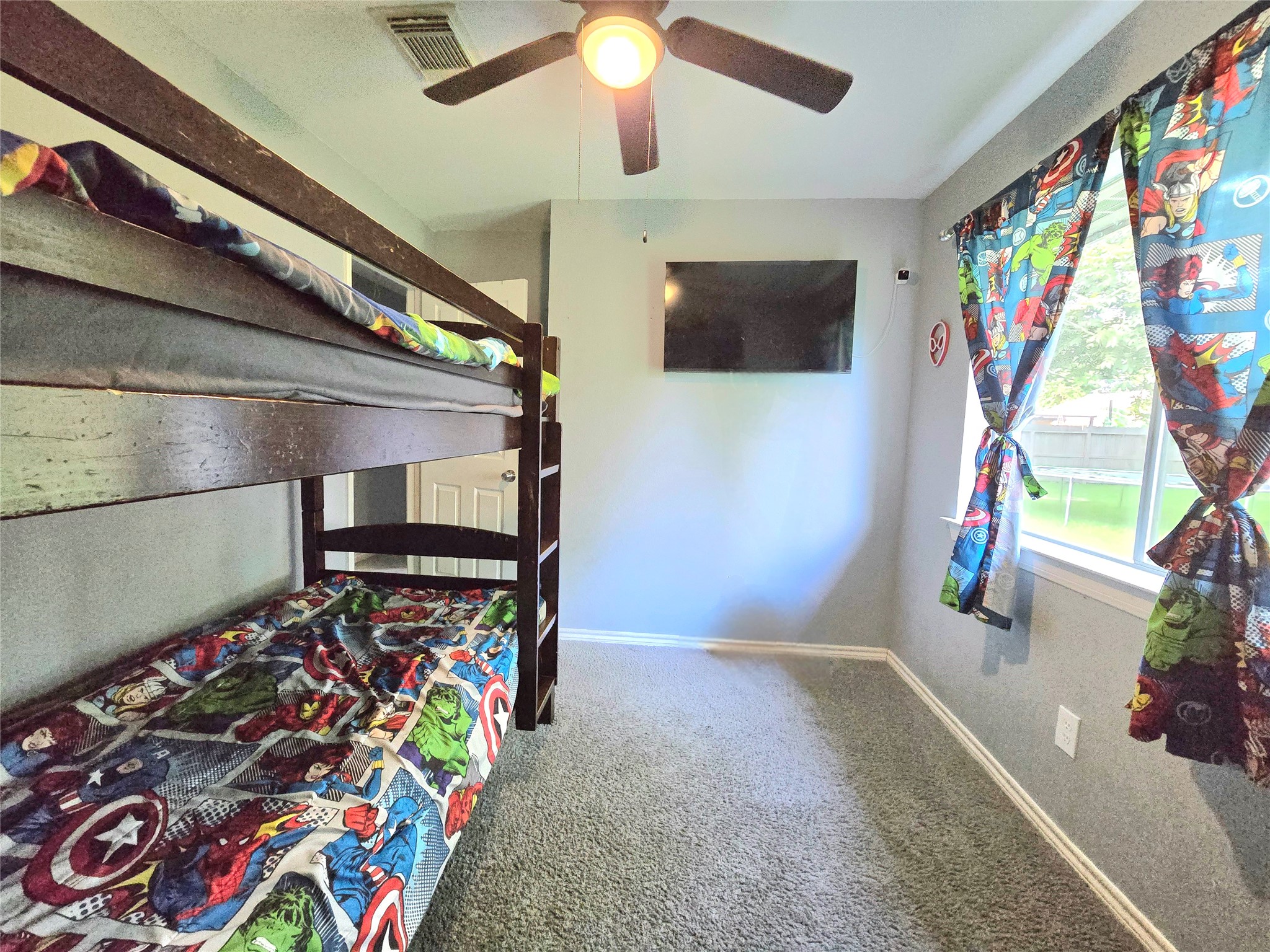 Charming bedroom with cozy bunk beds, vibrant superhero-themed decor, and a large window providing ample natural light.