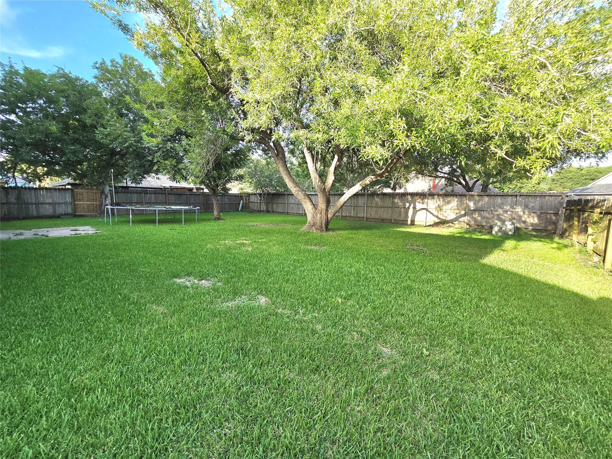 Spacious backyard featuring lush green grass, mature trees, and a wooden fence, offering ample space for outdoor activities and relaxation.