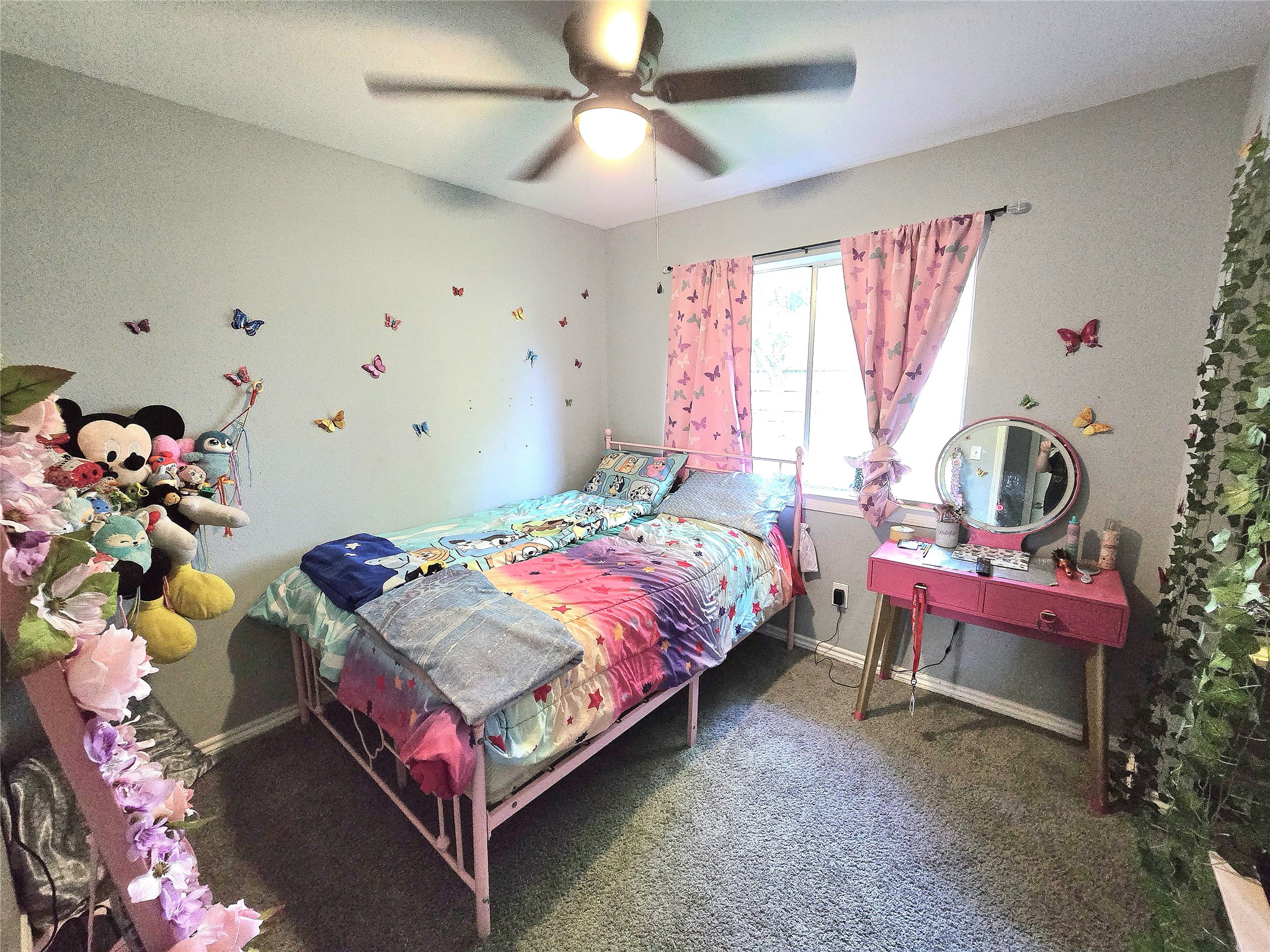 Charming bedroom with vibrant decor, featuring butterfly wall accents and a cozy bed, complemented by a vanity and a window for natural light.