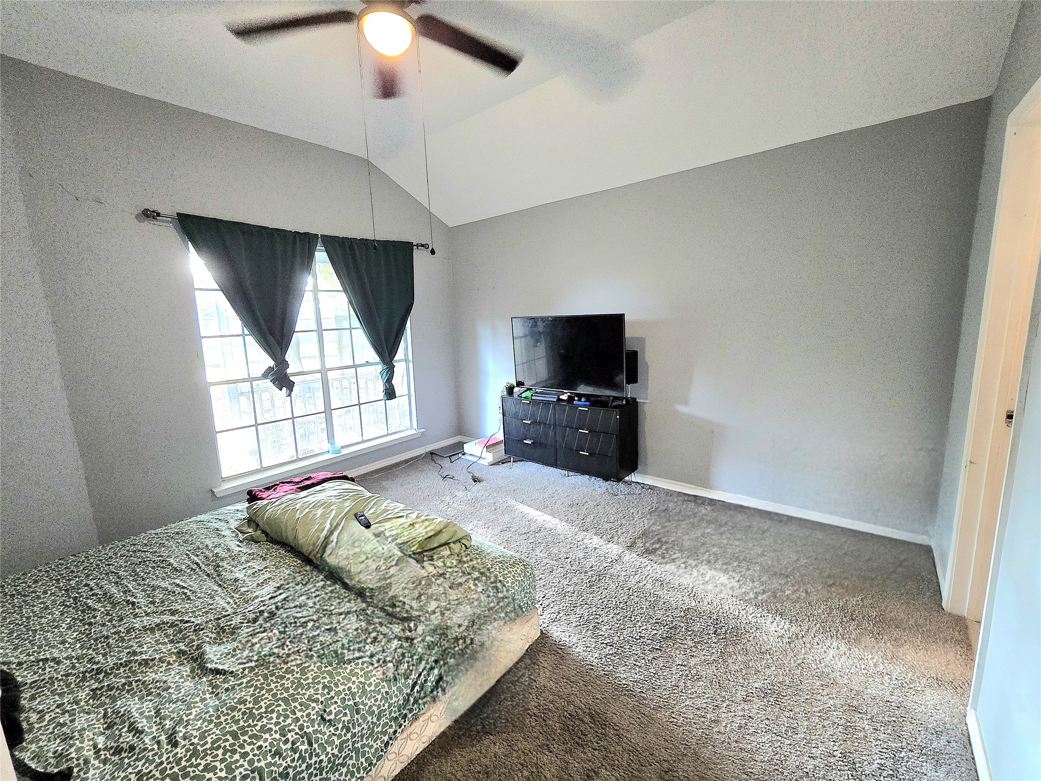 Spacious bedroom with vaulted ceilings, large window for natural light, and a ceiling fan for comfort.