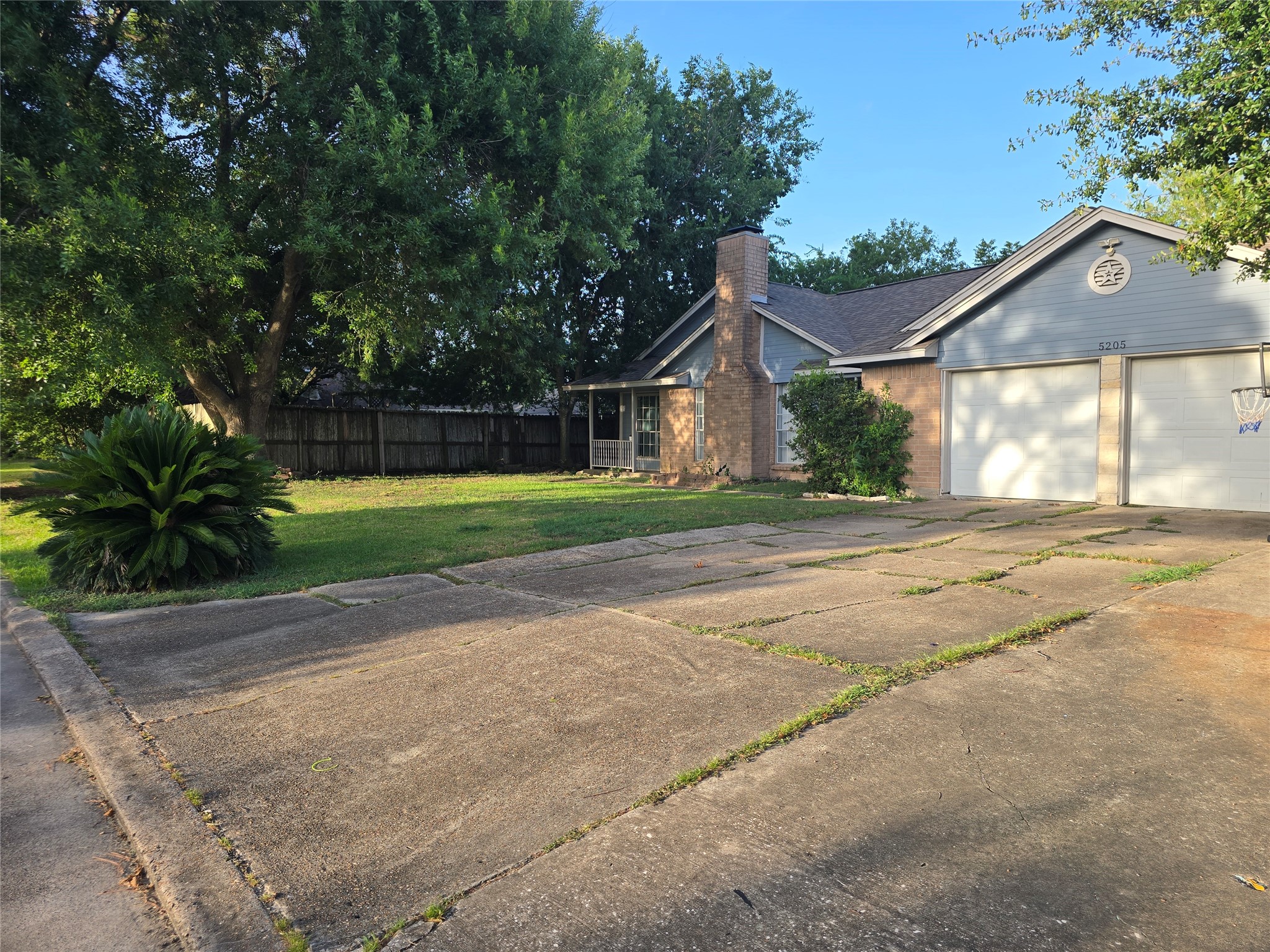 Charming single-story home with a spacious driveway, attached garage, and a lush front yard accented by mature trees and well-kept landscaping.