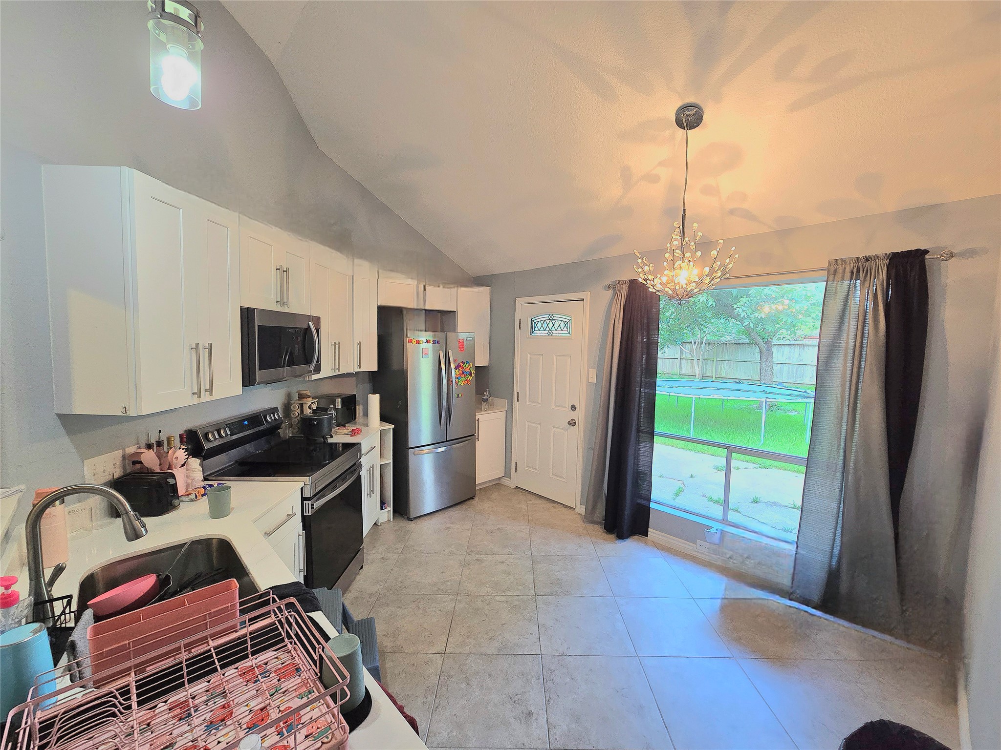 Bright kitchen features modern appliances, sleek cabinetry, and a stylish chandelier, with a view of the backyard through large windows.