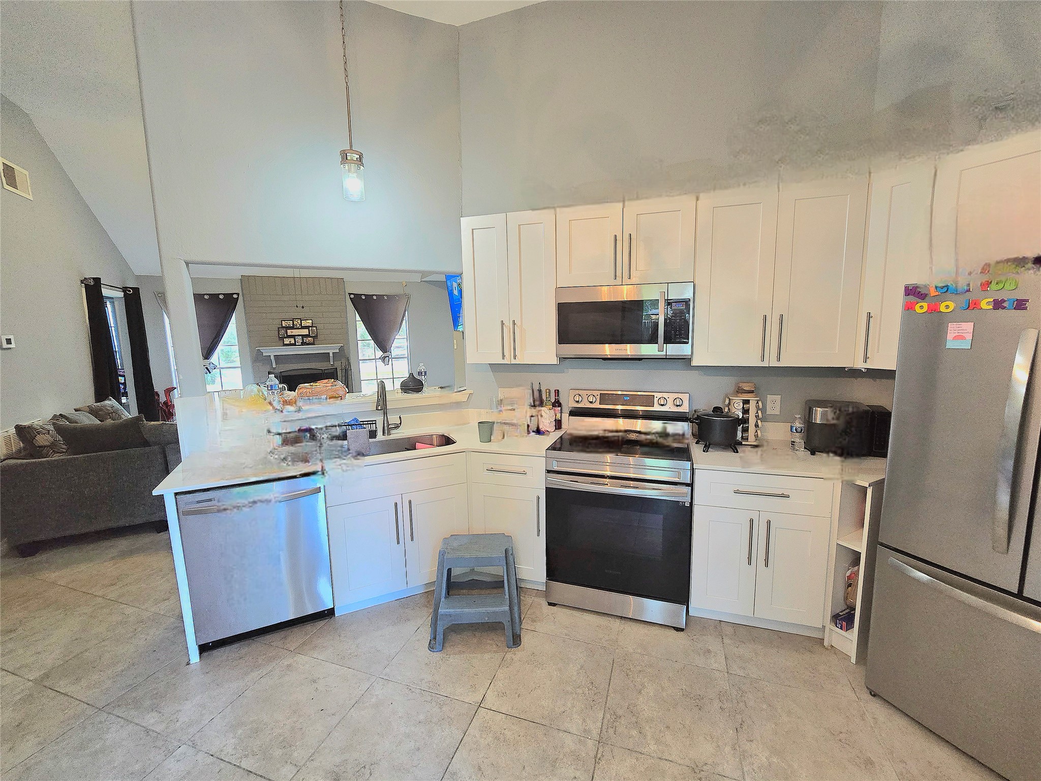 Modern kitchen with sleek stainless steel appliances, white cabinetry, and open access to a cozy living area featuring a fireplace.