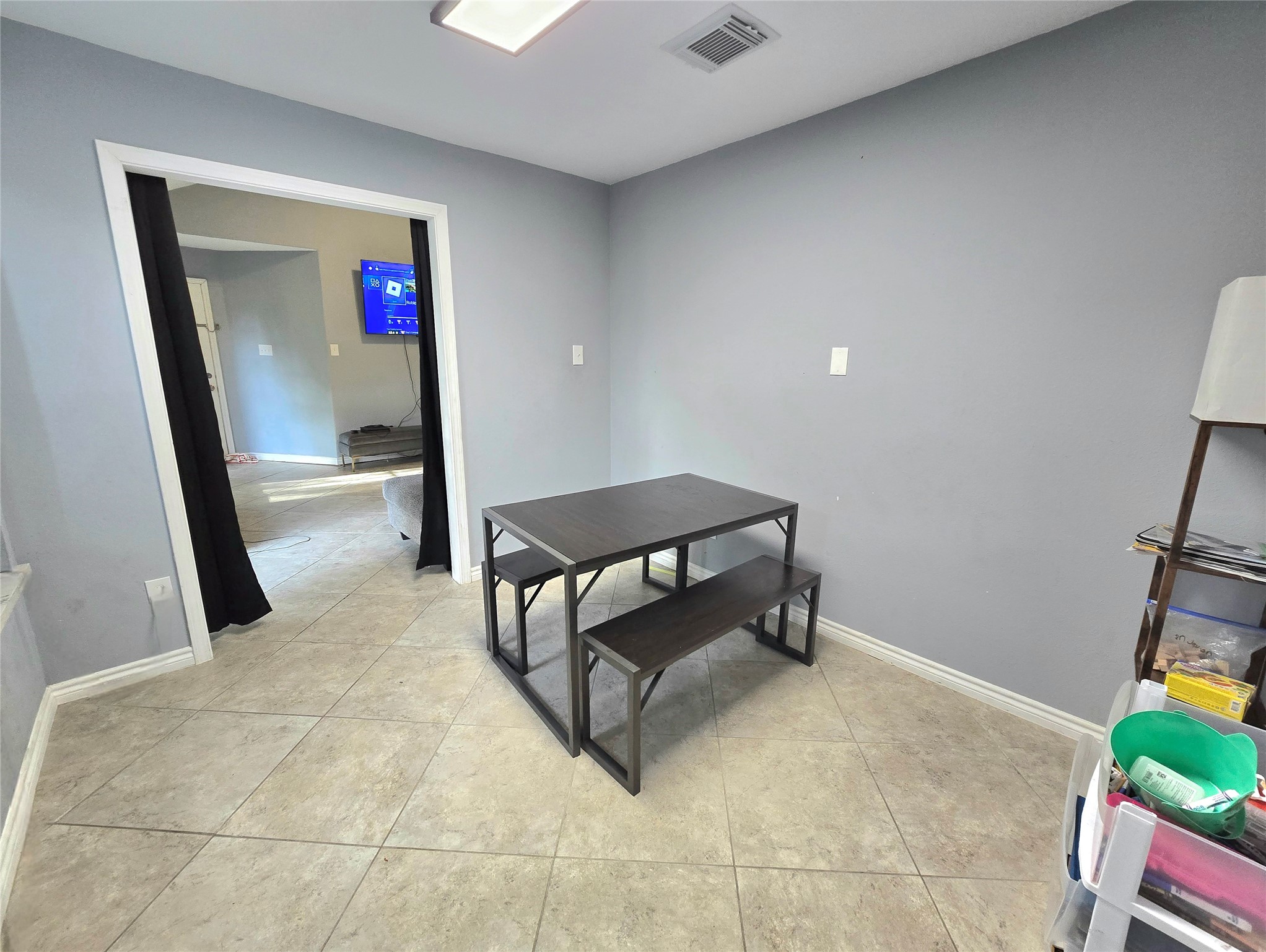 Bright and inviting room with sleek tile flooring, featuring a cozy dining area and a view into an adjoining space, perfect for gatherings.