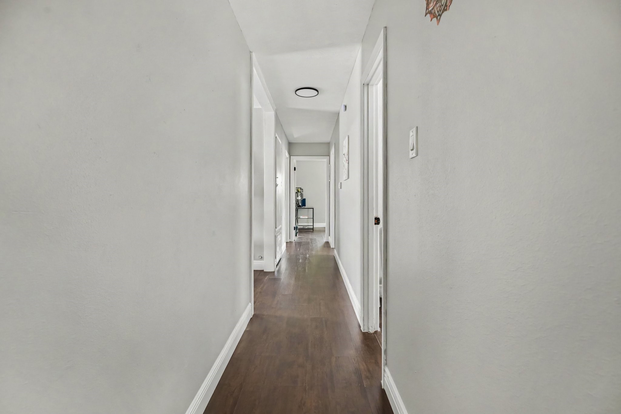 Bright, inviting hallway connecting living areas featuring elegant floors and crisp white walls, leading to all bedroom and bathrooms.