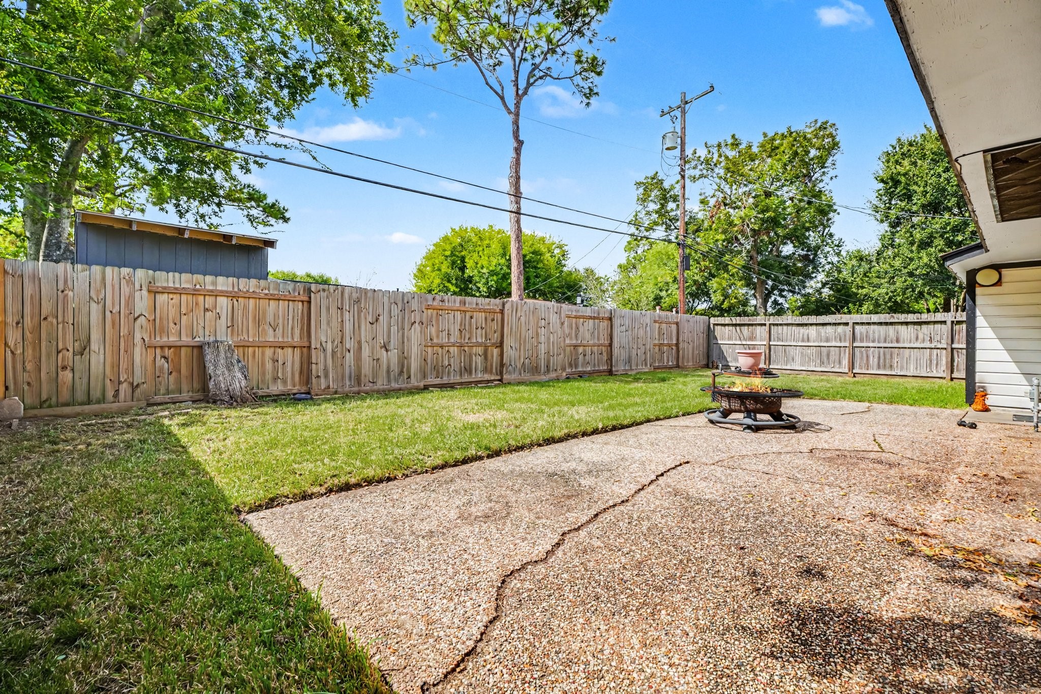 Spacious backyard with a blend of grassy and paved areas, perfect for outdoor gatherings, enclosed by a tall wooden fence for privacy.
