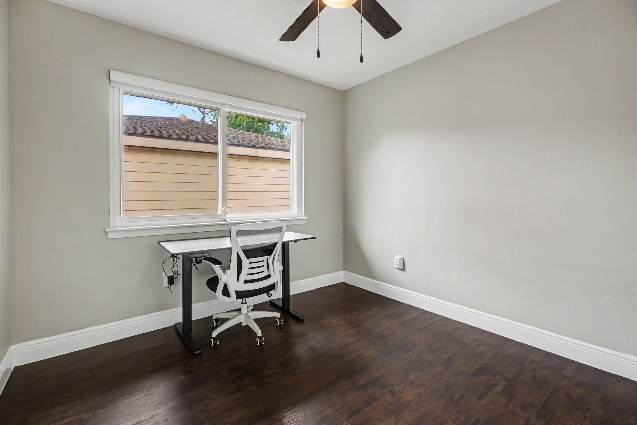 Bedroom Two featuring a large window, sleek desk, comfortable chair, and stylish ceiling fan, all set against rich laminate flooring.