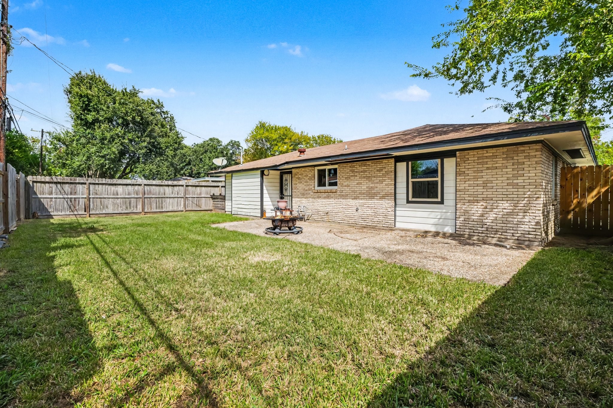 Spacious backyard with a mix of lush grass and a paved patio, perfect for outdoor activities and relaxation, bordered by a sturdy wooden fence for privacy.