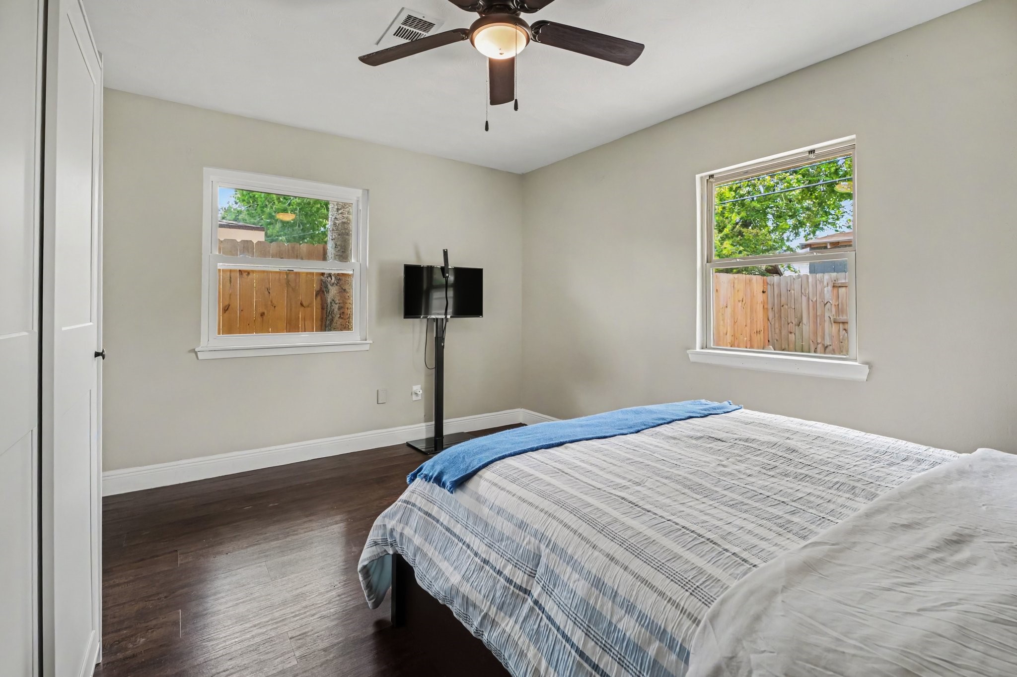 Primary bedroom featuring hardwood floors, ample natural light from two windows, and a ceiling fan for comfort.