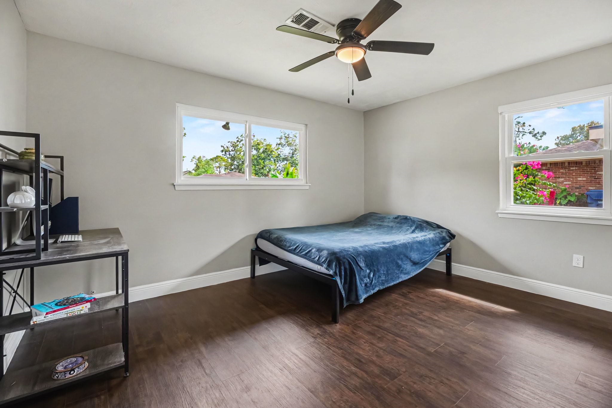 Bedroom One with laminate floors, featuring a ceiling fan, ample natural light from two windows, and a spacious layout ideal for relaxation or work.