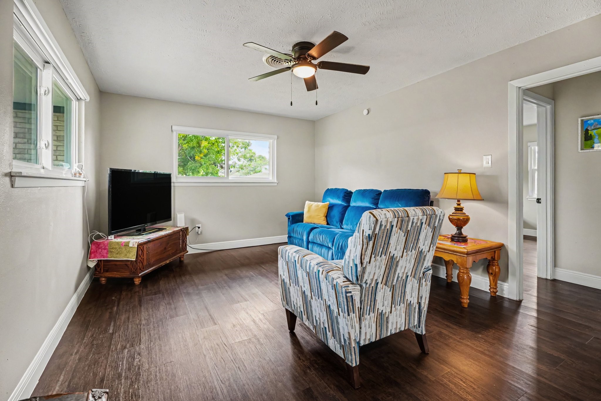 Cozy living room featuring hardwood floors, a ceiling fan, and abundant natural light, perfect for relaxation and entertainment.