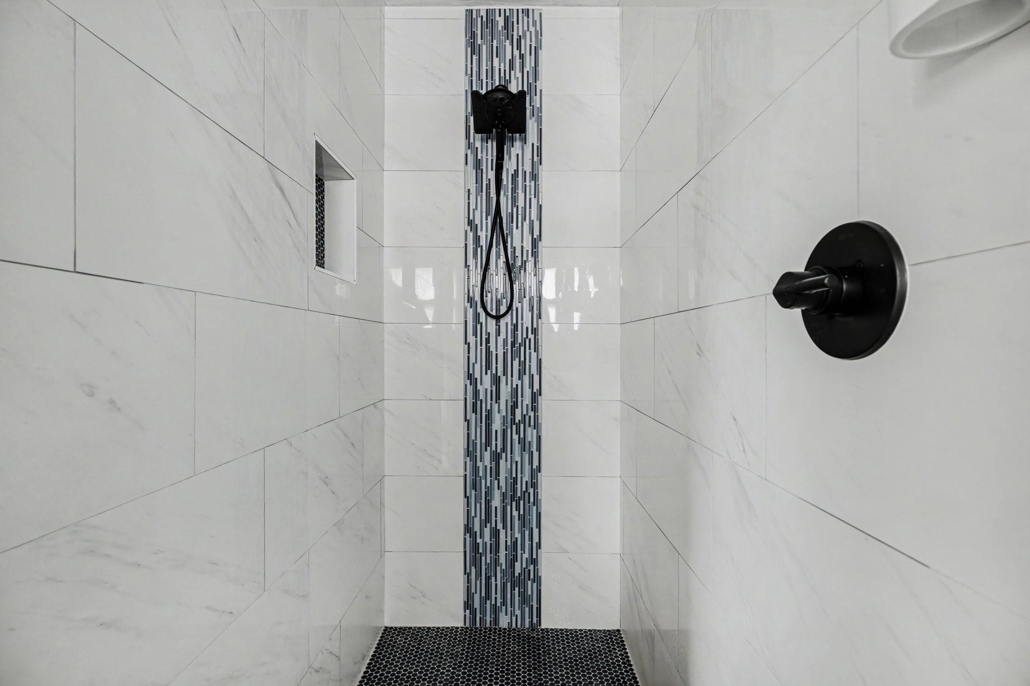 Primary shower with sleek white tile, a striking vertical mosaic accent, and modern black fixtures for a luxurious touch.