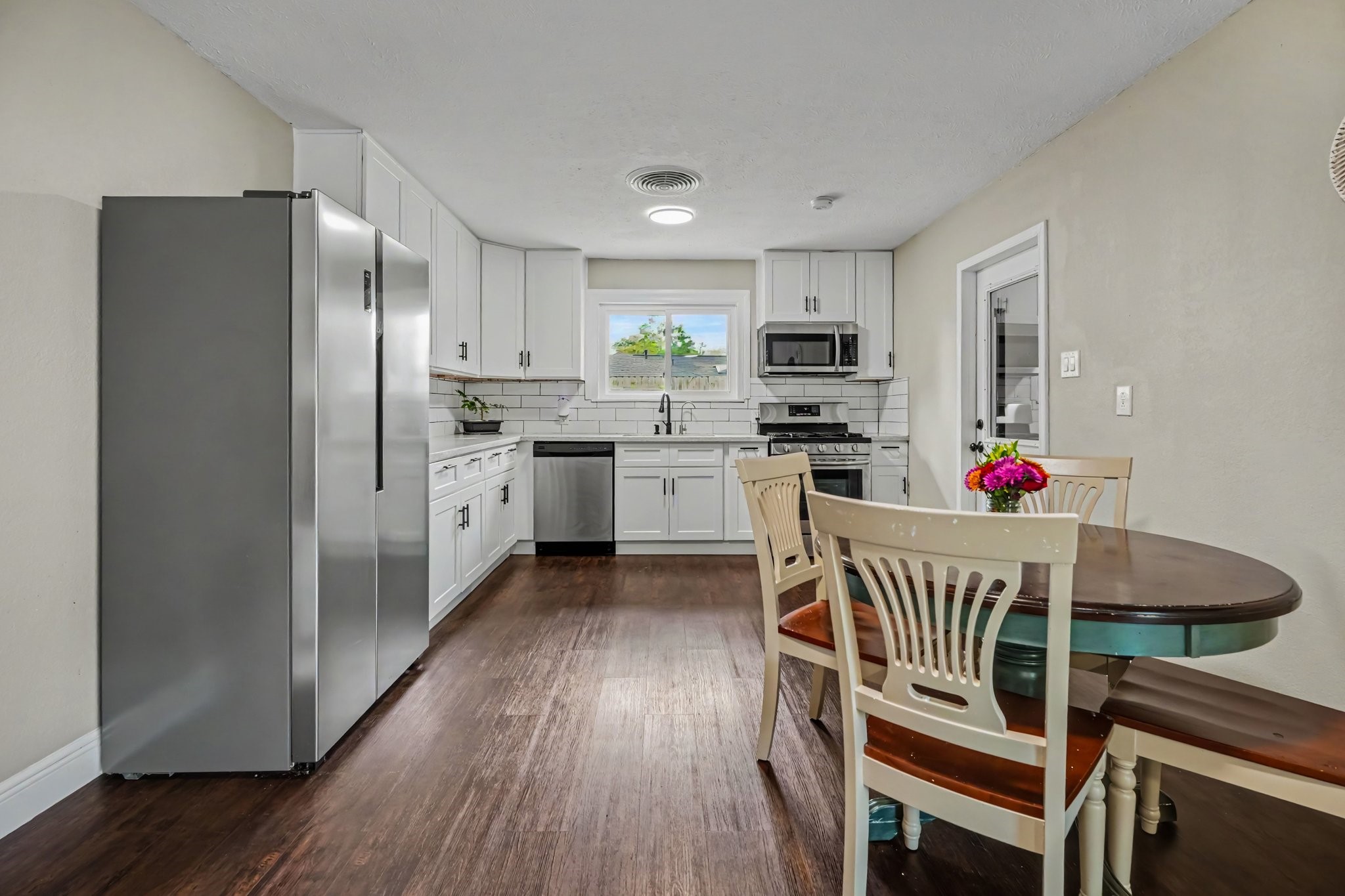 Bright and spacious kitchen with modern stainless steel appliances, sleek white cabinetry, and laminate floors, complemented by a cozy dining area.
