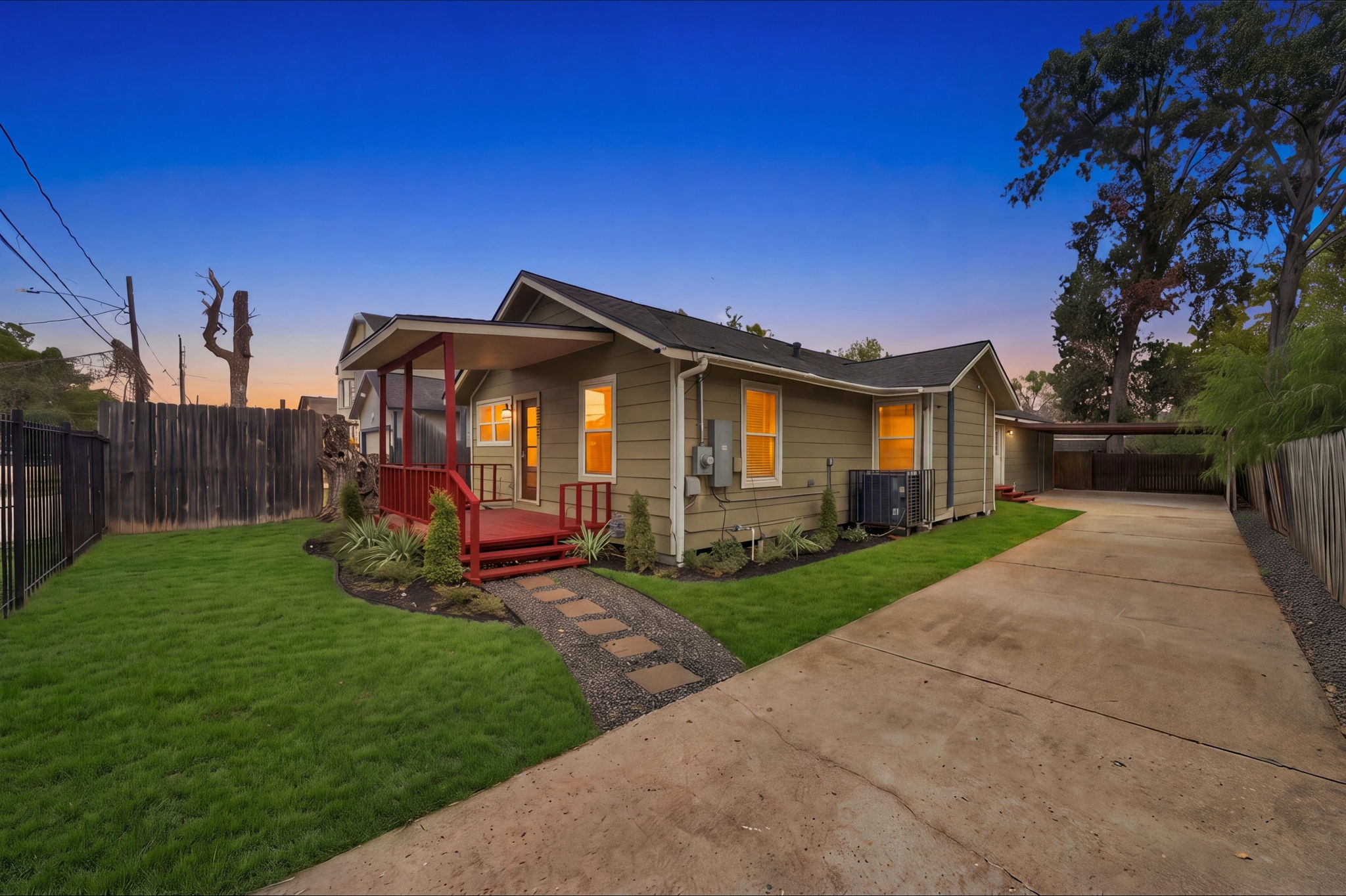 Charming single-story home with a welcoming front porch, vibrant landscaping, and a spacious driveway leading to a carport, set against a serene evening sky.