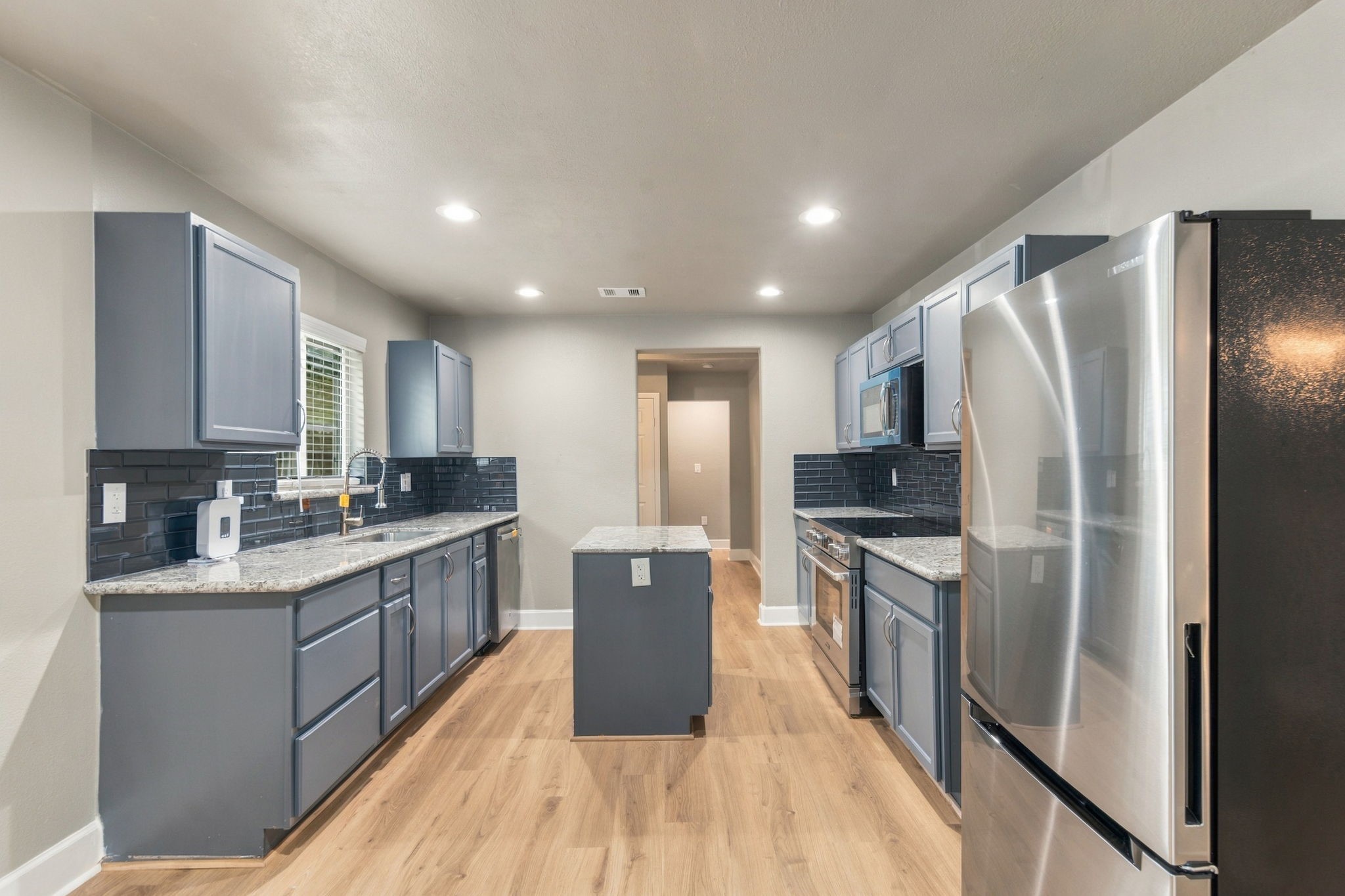 Modern kitchen with sleek stainless steel appliances, elegant granite countertops, and stylish gray cabinets complemented by a chic dark tile backsplash.